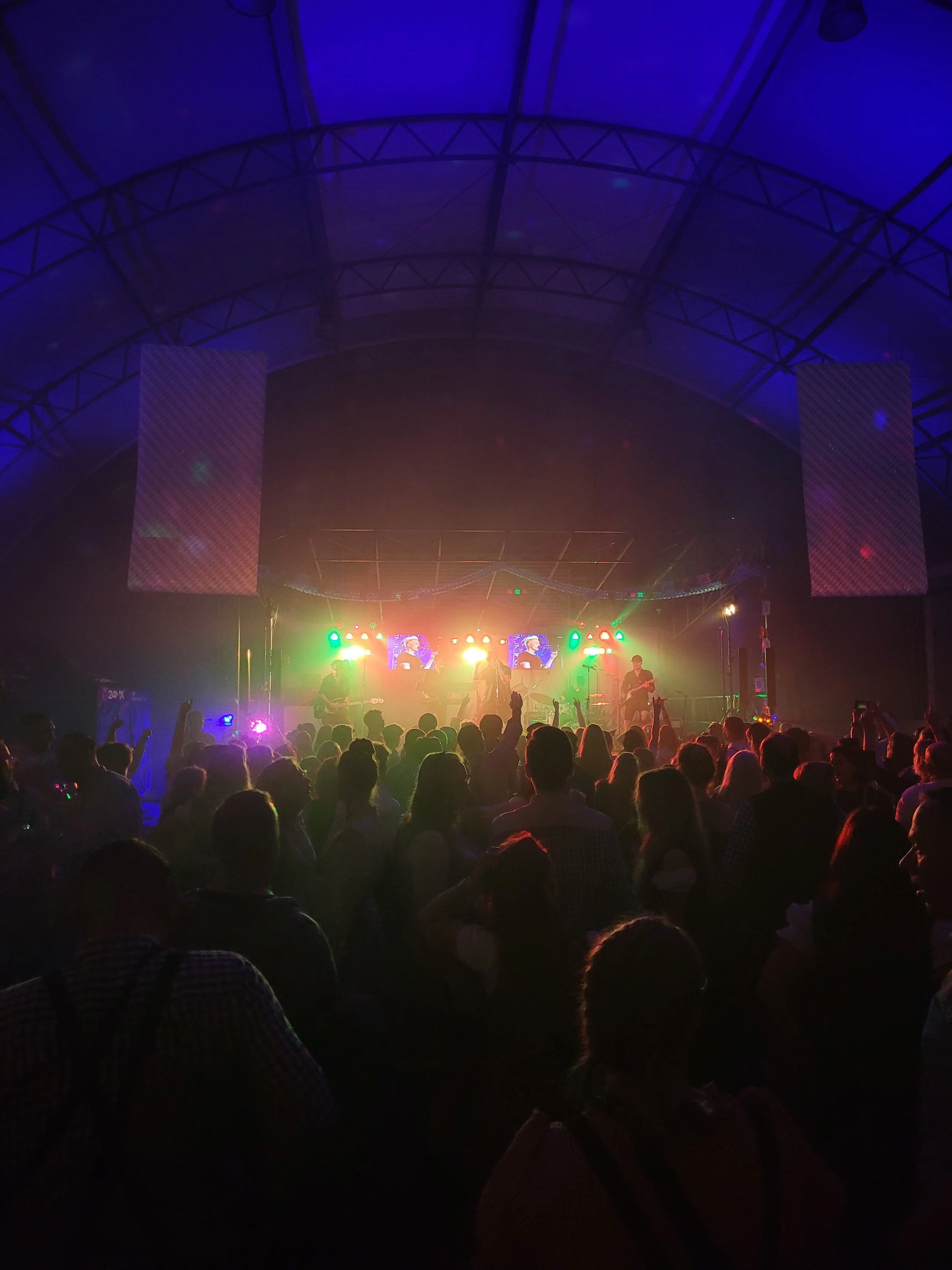 Crowd watching a live band perform on stage in a large indoor venue with colorful lights.