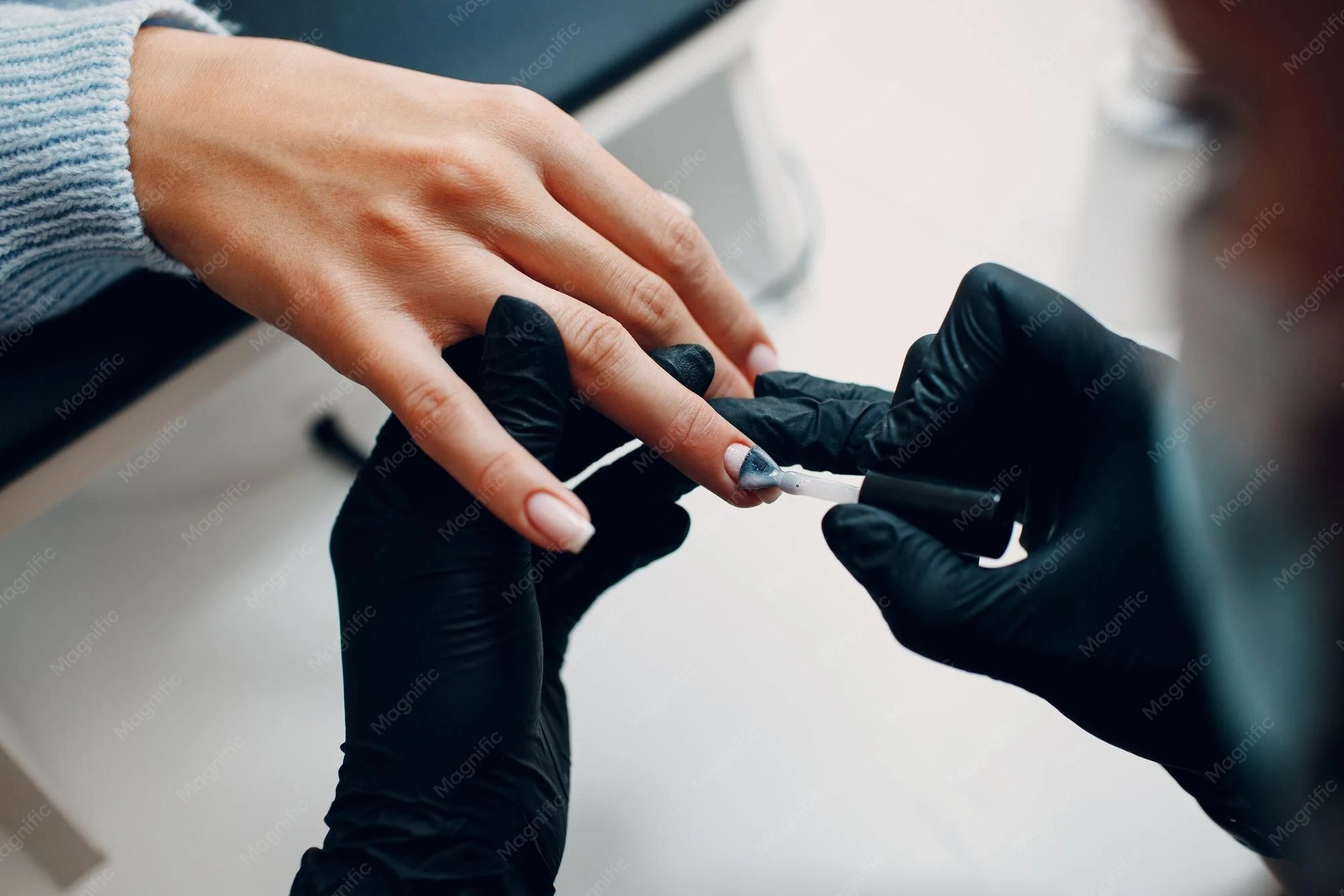 Persoon die een nagellakje aan een hand aanbrengt, met een zwarte handschoen op, professionele nagelverzorging.