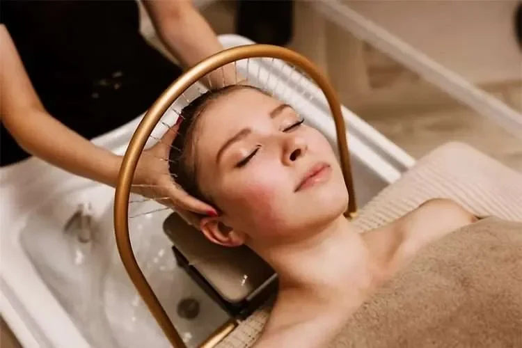 Vrouw krijgt een pedicurebehandeling in een spa of salon, liggend met een warme handdoek over haar schouders, terwijl een specialist haar hoofd vasthoudt.