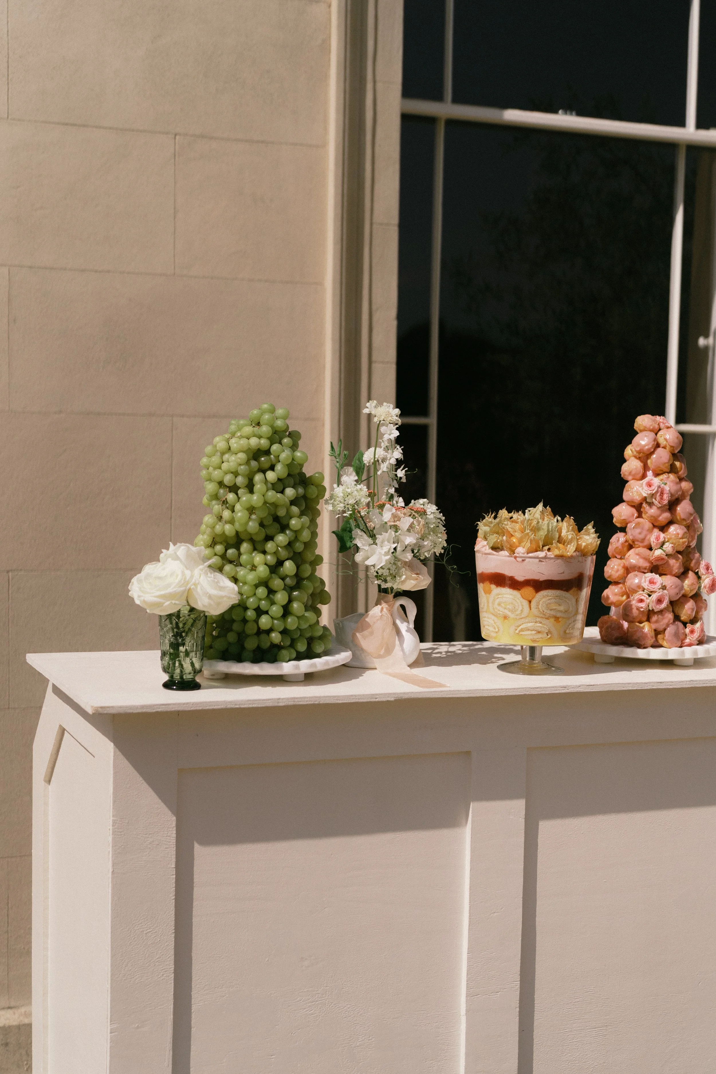 A white table with candles and a floral arrangement. In the background, there is a window with a dark night sky outside.