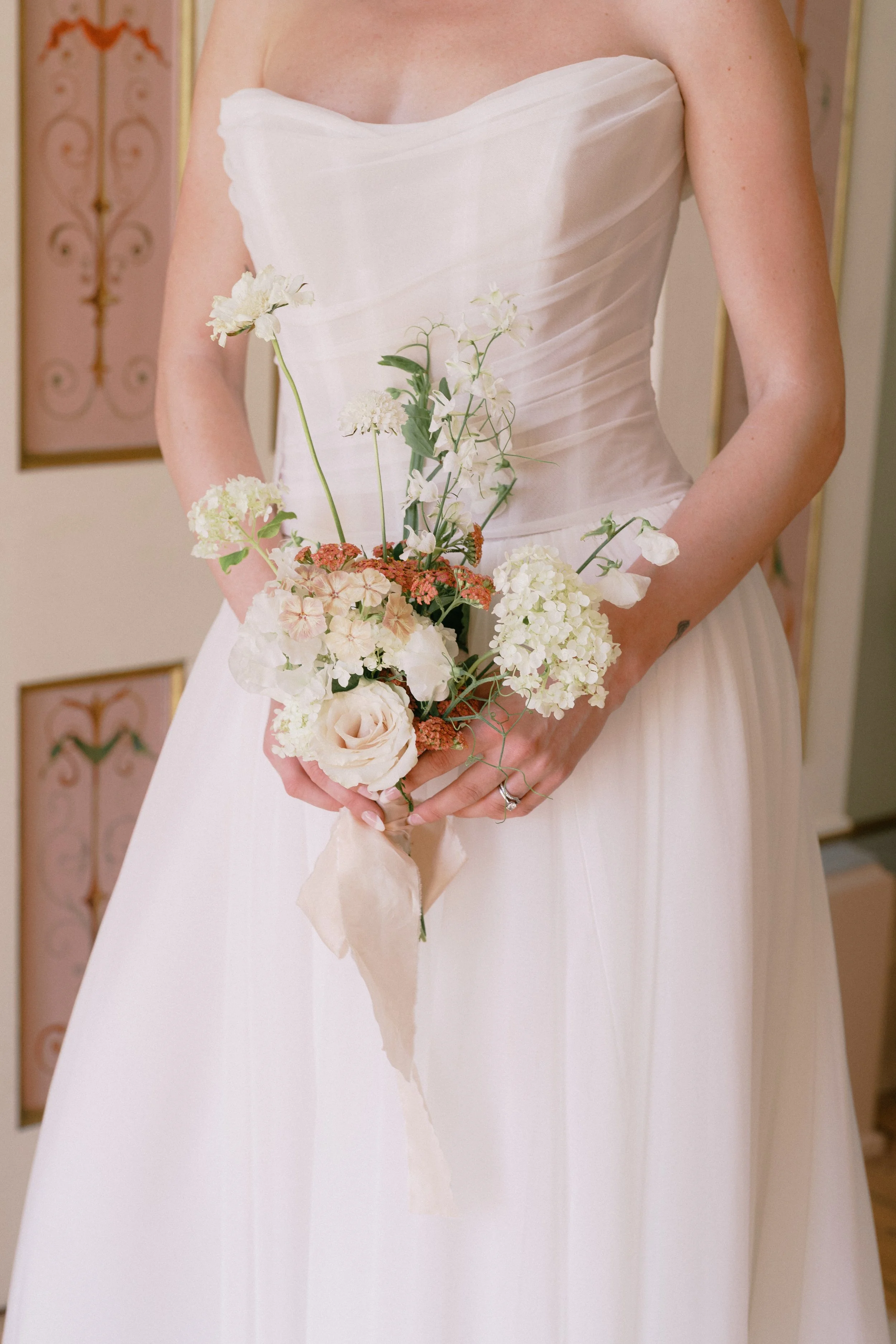 Close-up of a woman in a white wedding dress holding a bouquet of white, pink, and green flowers.