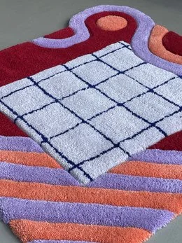 A colorful towel with orange, purple, and pink striped borders and a central section with a white grid pattern, draped over a surface.