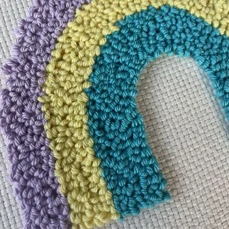 Close-up of colorful crocheted rainbow motifs in purple, yellow, and teal, arranged on a white woven surface.
