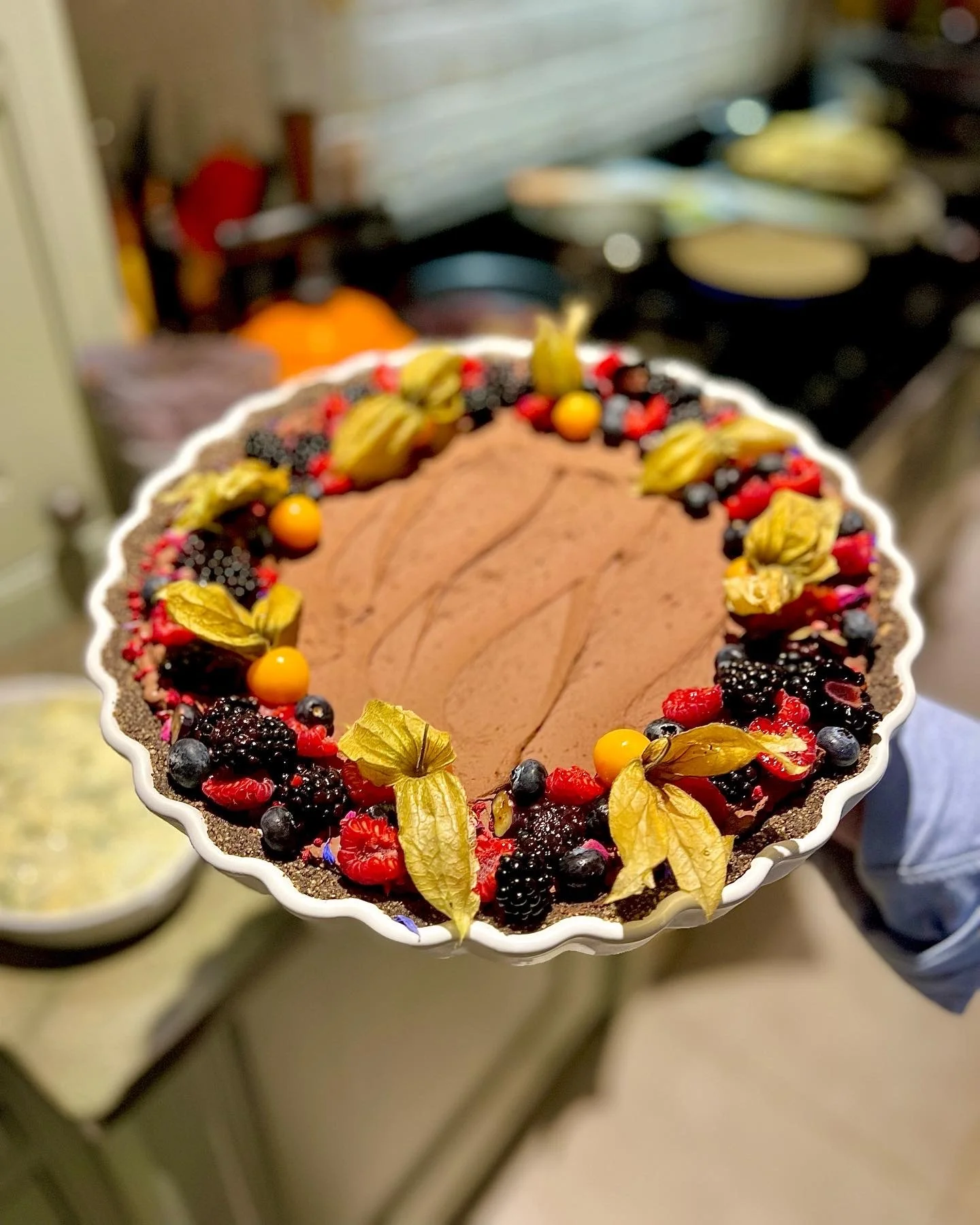 A chocolate tart decorated with various berries and physalis fruits.