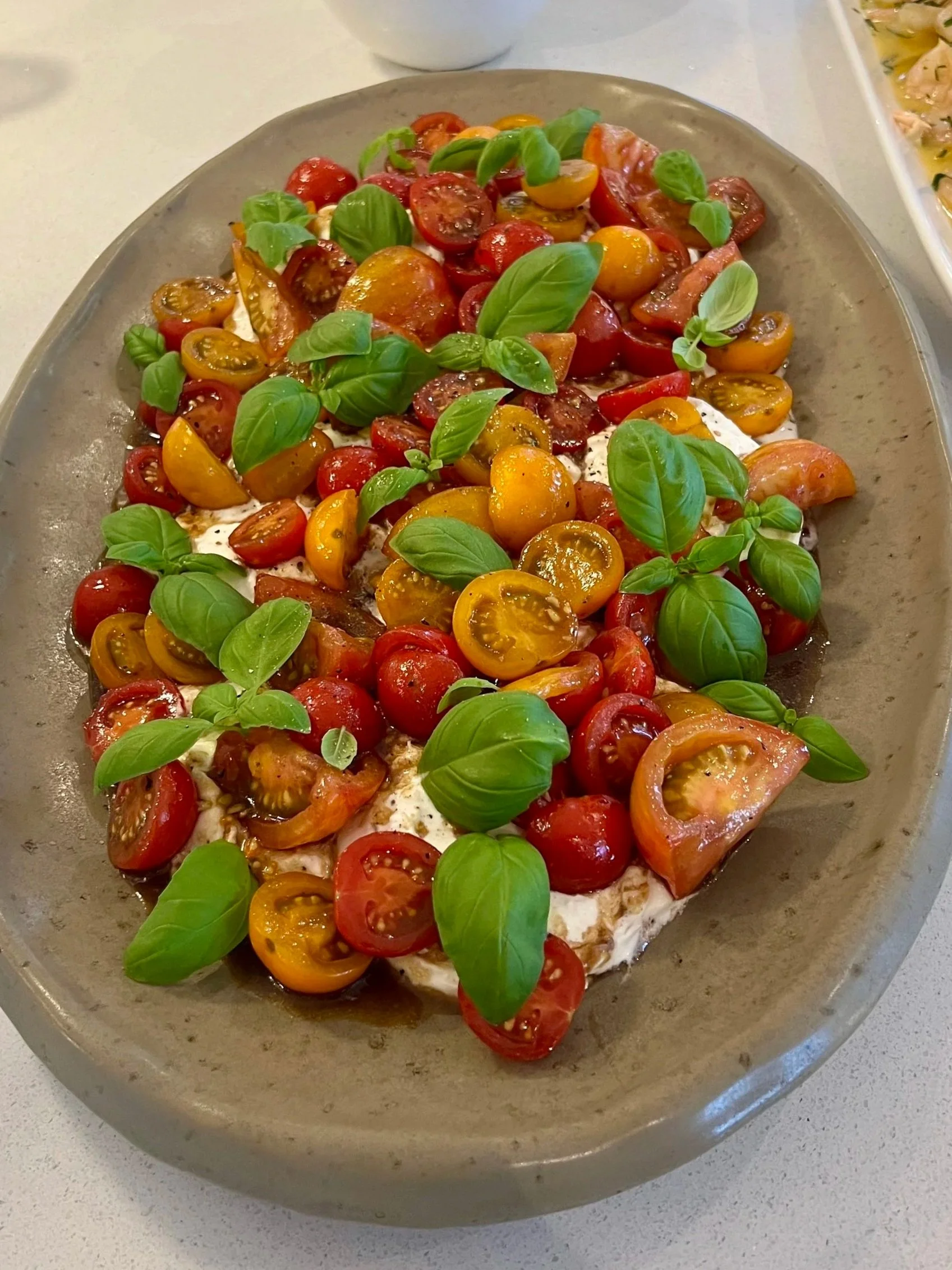 A salad with halved cherry tomatoes and fresh basil leaves on a gray plate.
