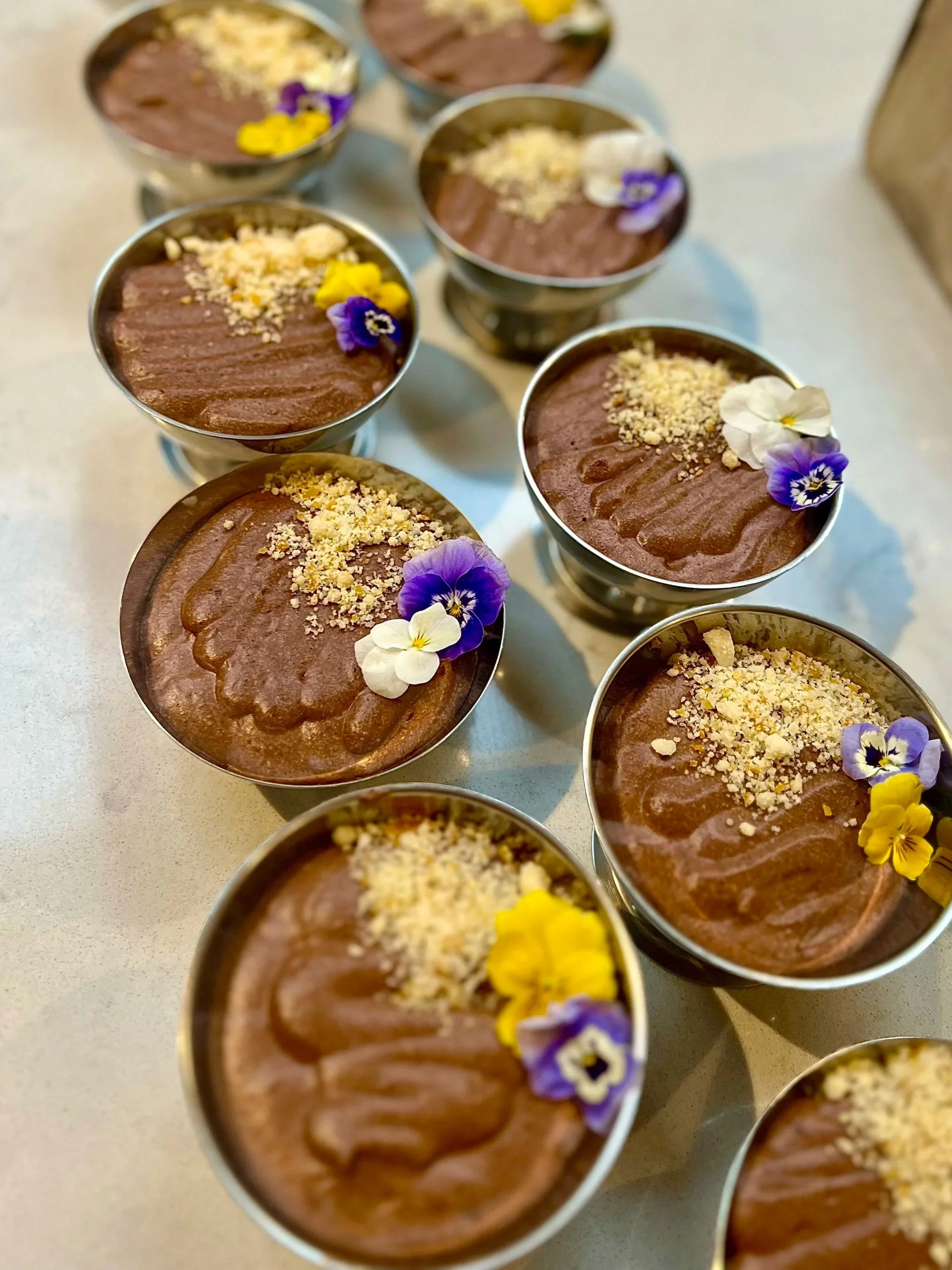 Chocolate mousse cups garnished with edible flowers and crushed nuts.
