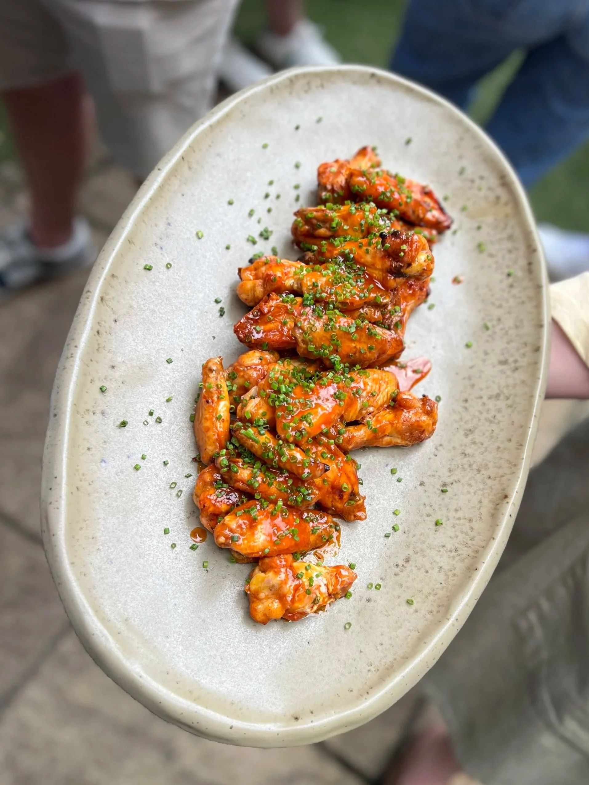 Close-up of a plate with glazed chicken wings garnished with chopped chives.