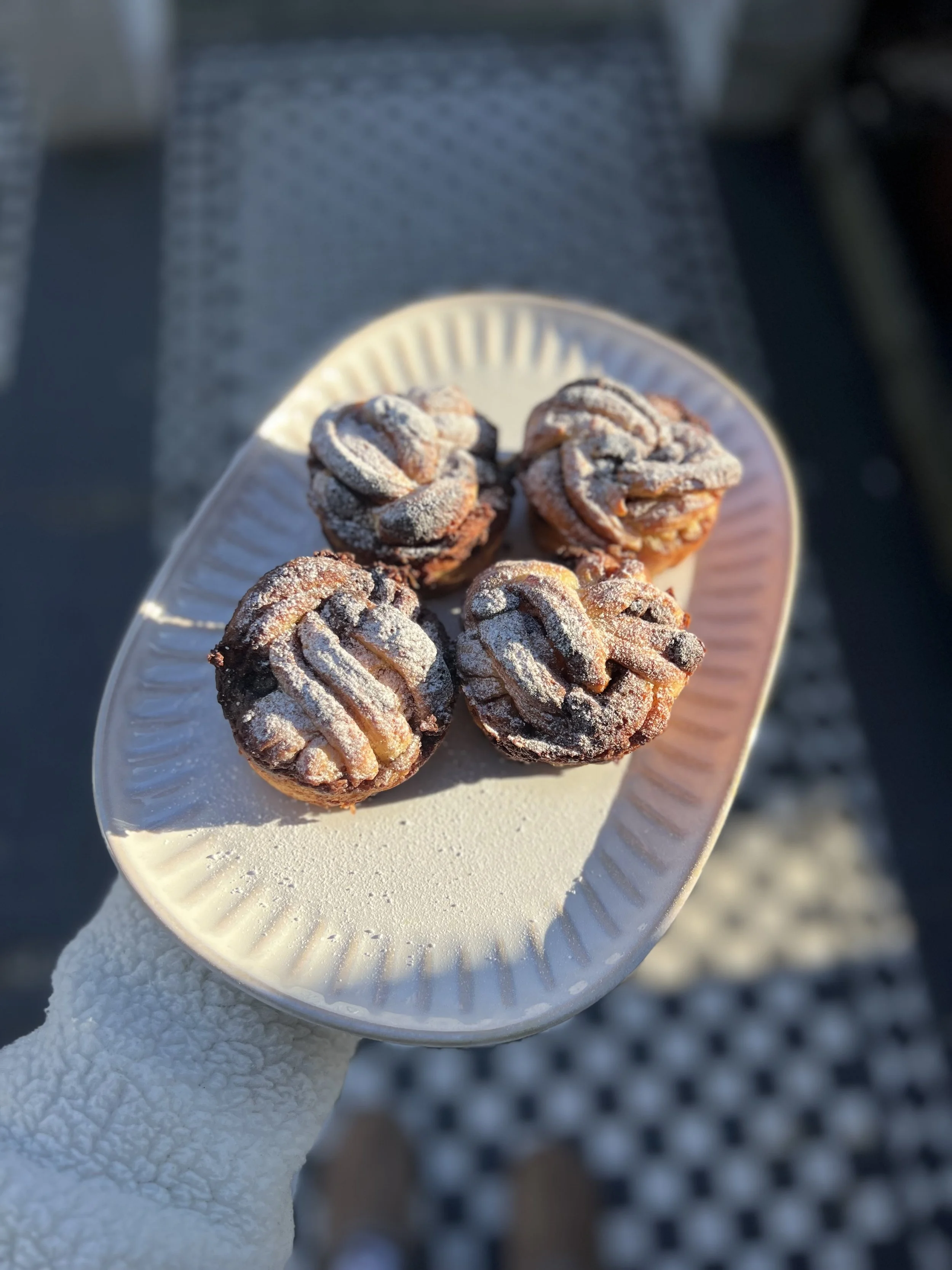 Close-up of a paper plate with several Easter egg cookies, dusted with powdered sugar, held by a gloved hand outside on a checkered table.