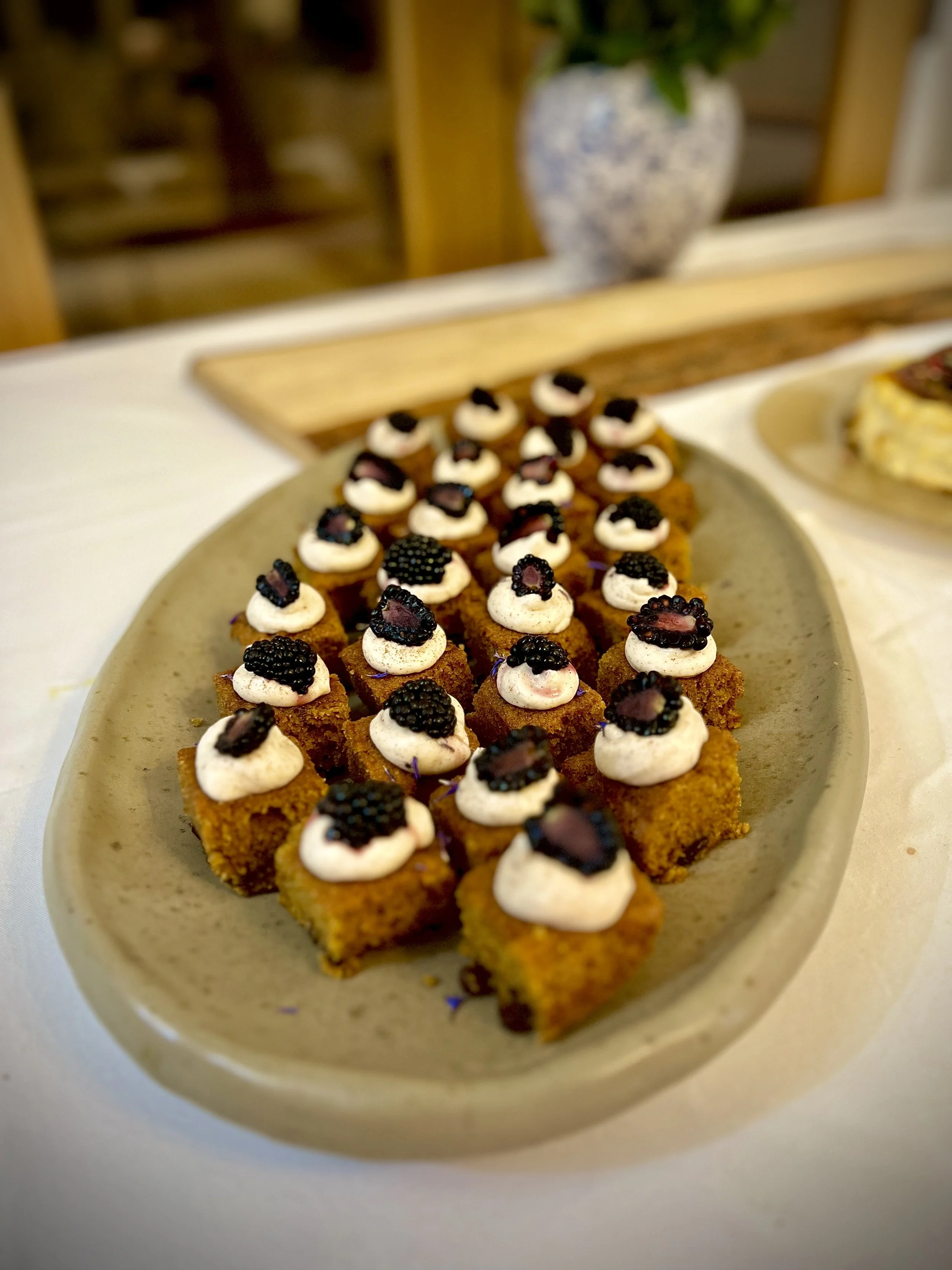 Plate of small square baked goods topped with white cream and blackberries, displayed on a ceramic dish.