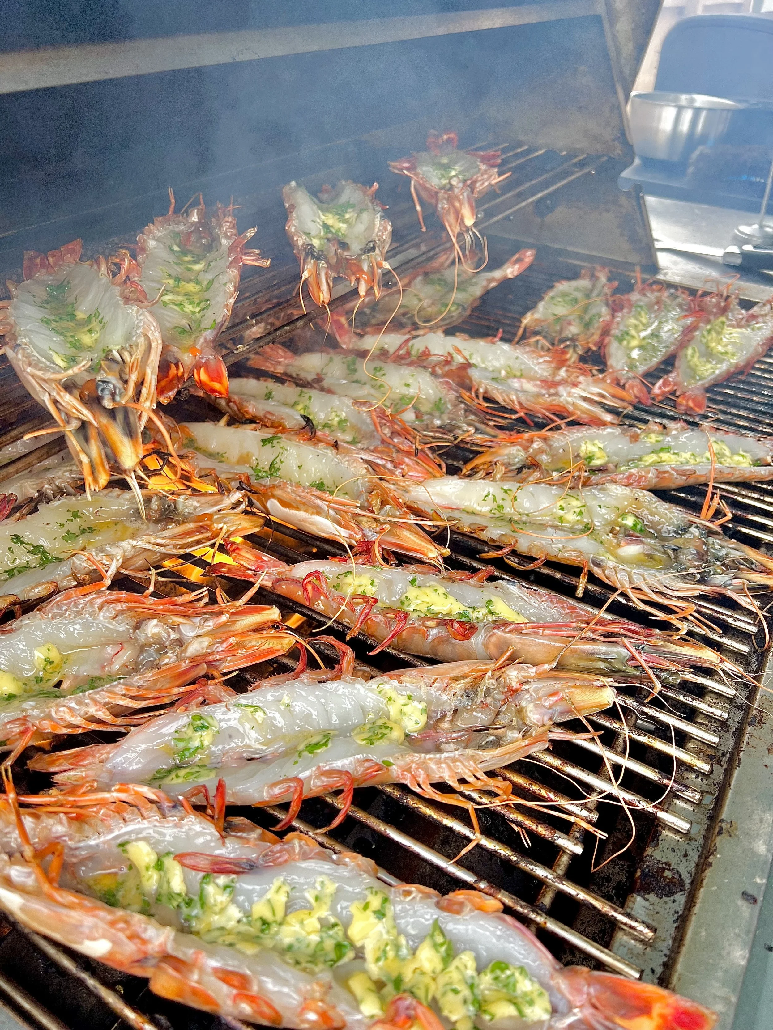 Large prawns or shrimp being grilled on an outdoor barbecue grill, stuffed with herbs and vegetables.
