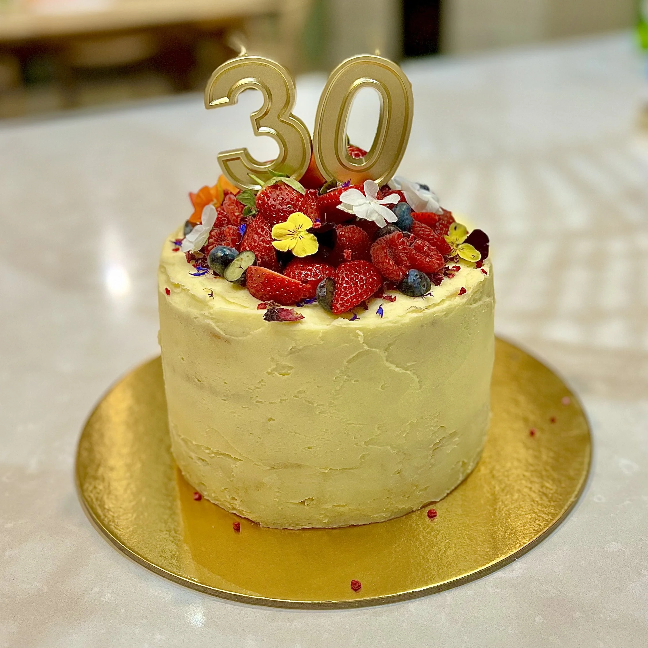 A birthday cake with strawberry and edible flowers topped with a gold '30' candle.