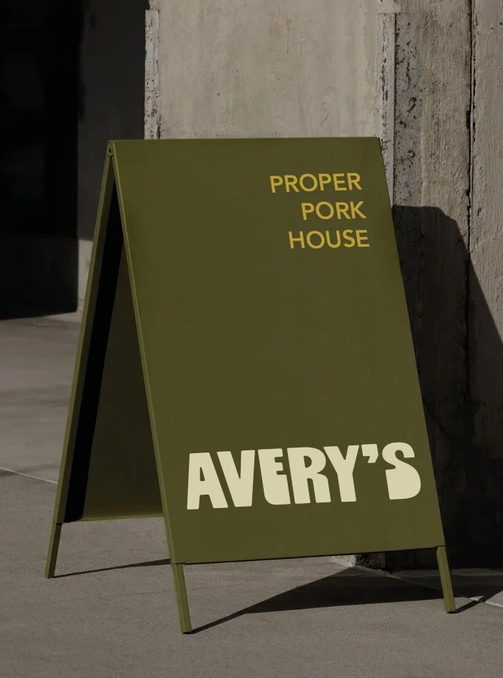 Green sandwich board sign outside a restaurant with yellow and white text that reads 'Proper Pork House' and 'Avery's'.
