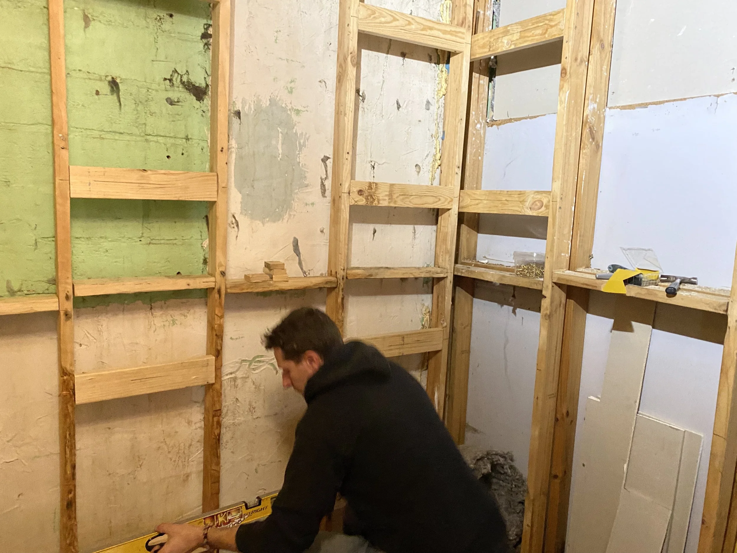 A person working on a wooden framing project in an unfinished room, with tools and materials around.