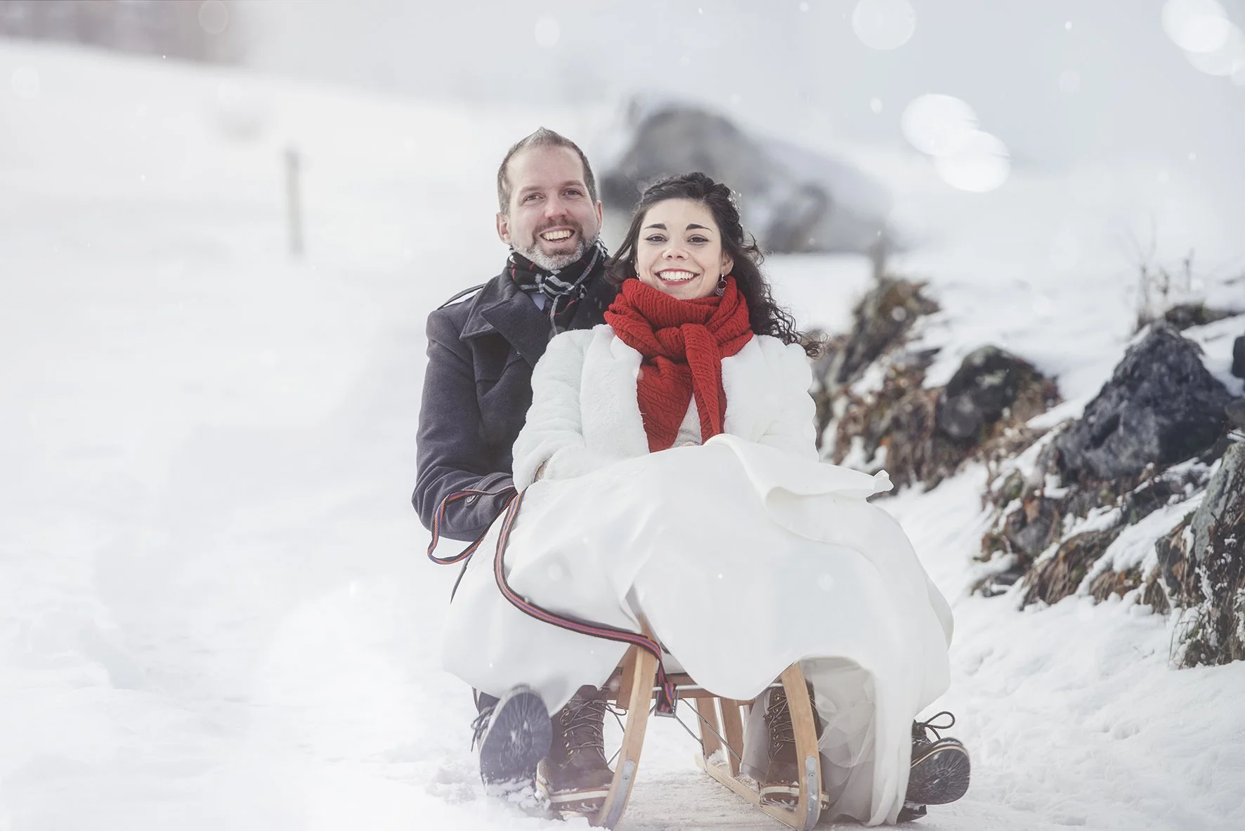 Ein lachendes Paar fährt auf einem Schlitten durch verschneite Winterlandschaft.
