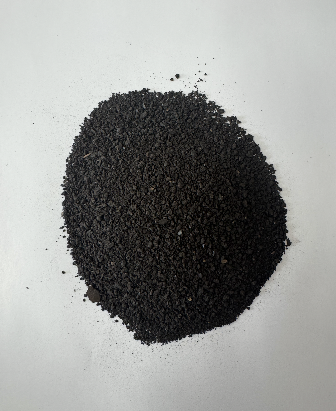 Pile of black granular material on a white surface.