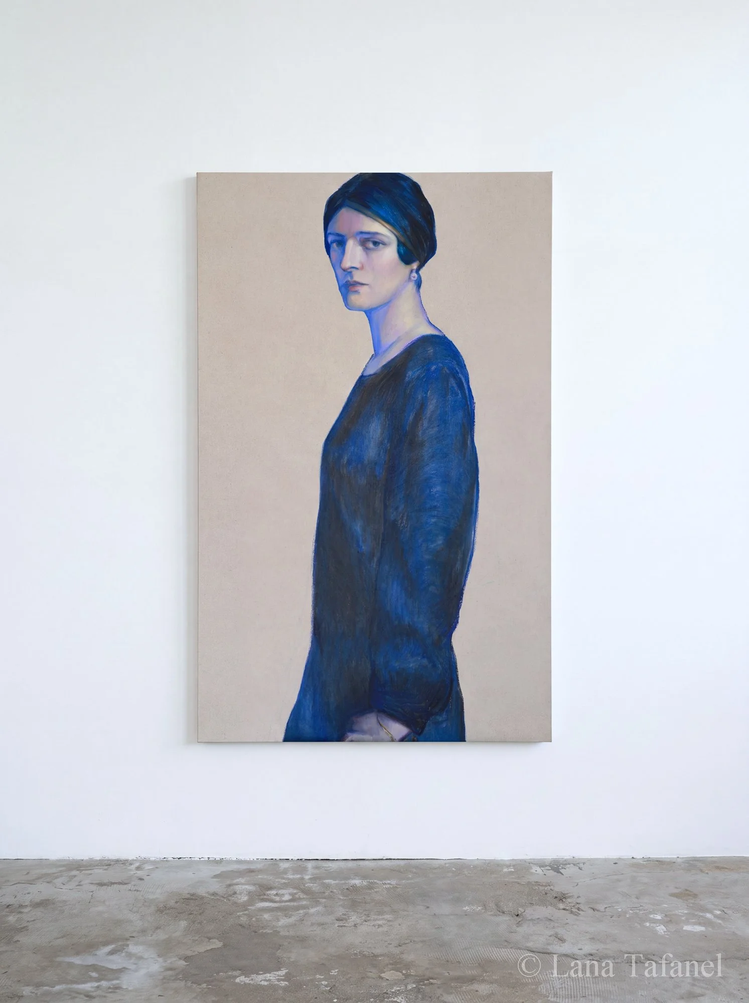 Portrait of a woman with dark hair styled in a side part, wearing a dark blue top, painted in a realistic style. The painting is hung on a plain white wall,. contemporary art