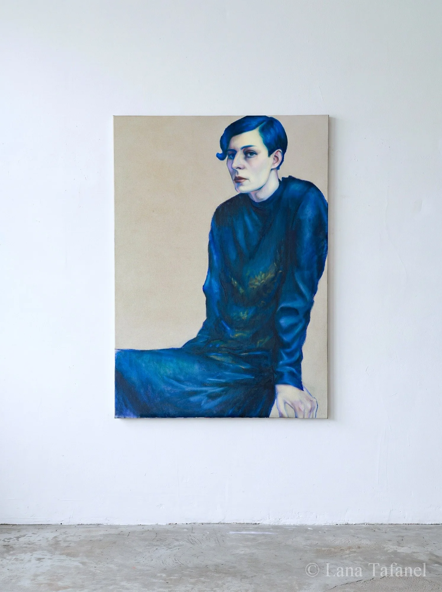 A portrait painting of a woman with short dark blue hair, wearing a dark top, sitting against a plain beige background, displayed on a white gallery wall.