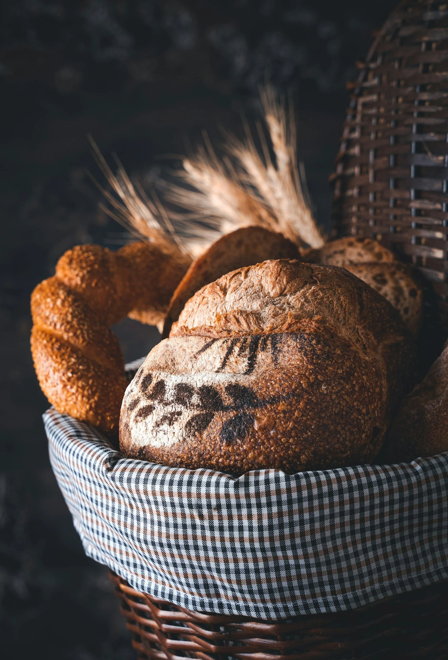 Assorted artisan loaves of crusty bread in a checkered-lined wicker basket with wheat stalks