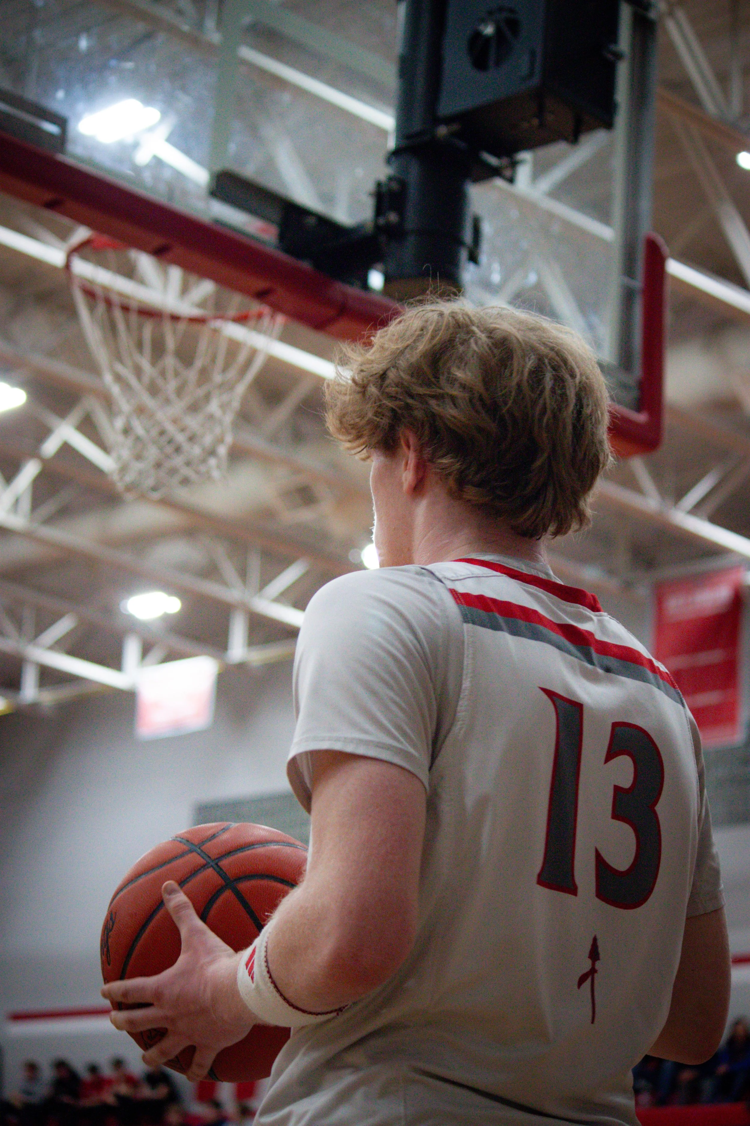 A basketball player holding a basketball, wearing a white jersey with the number 13, in an indoor basketball court.
