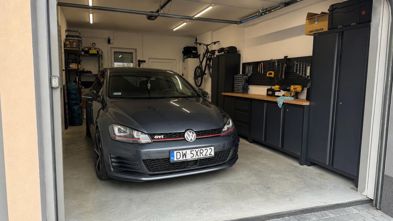Garaż samochodowy z Volkswagenem Golf GTI, podstawową zabudową warsztatową, blatem roboczym i ścianą na narzędzia.