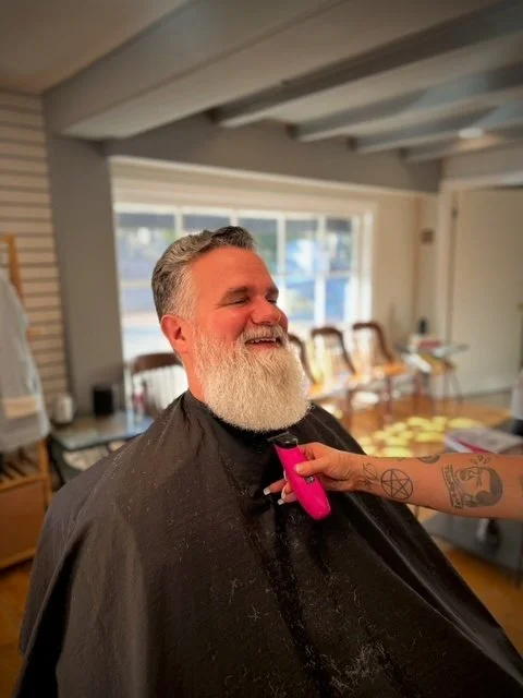 Smiling man with gray hair and beard getting a haircut in a salon.