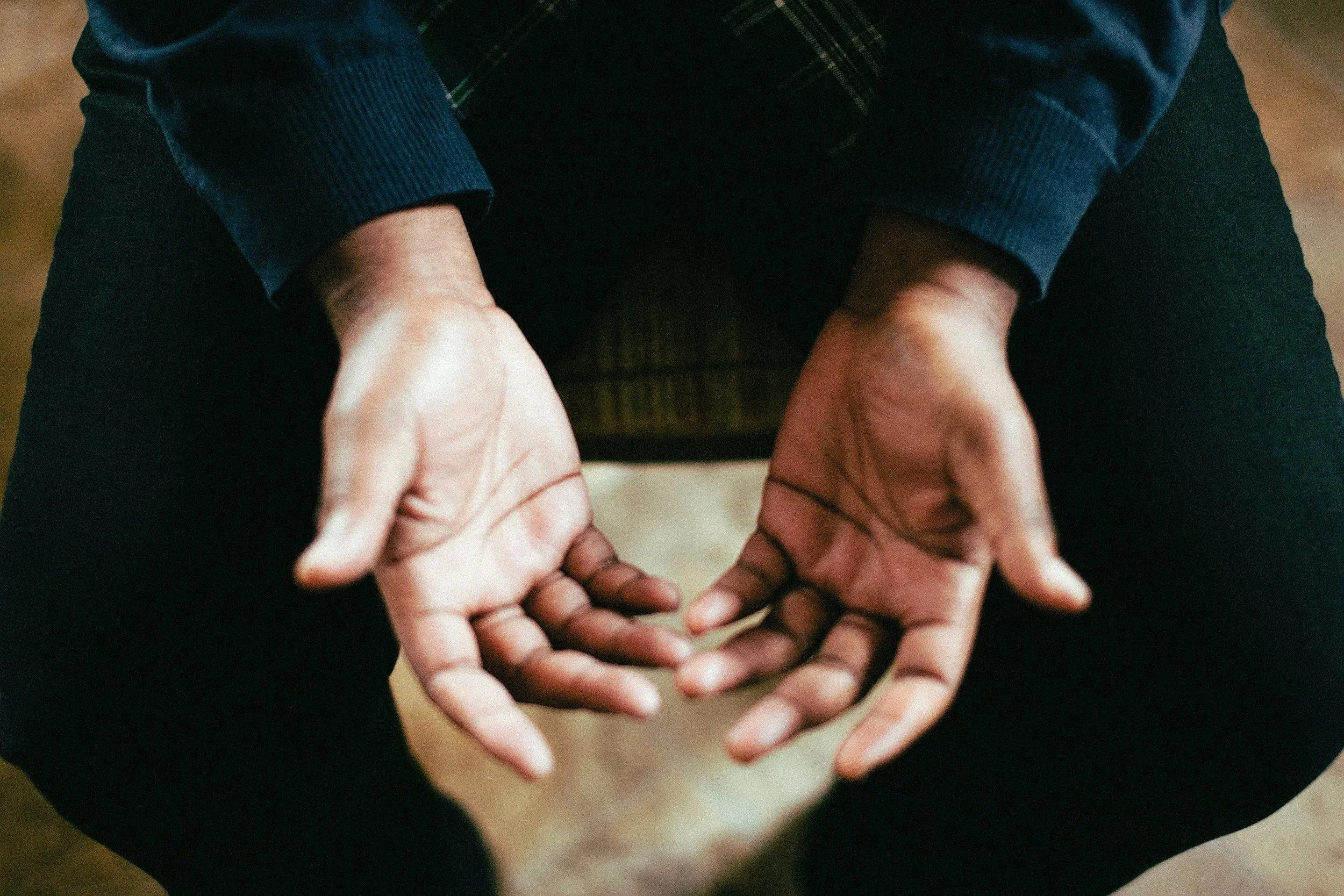 A person is sitting cross-legged on the ground, holding their hands together in a heart shape in front of them.