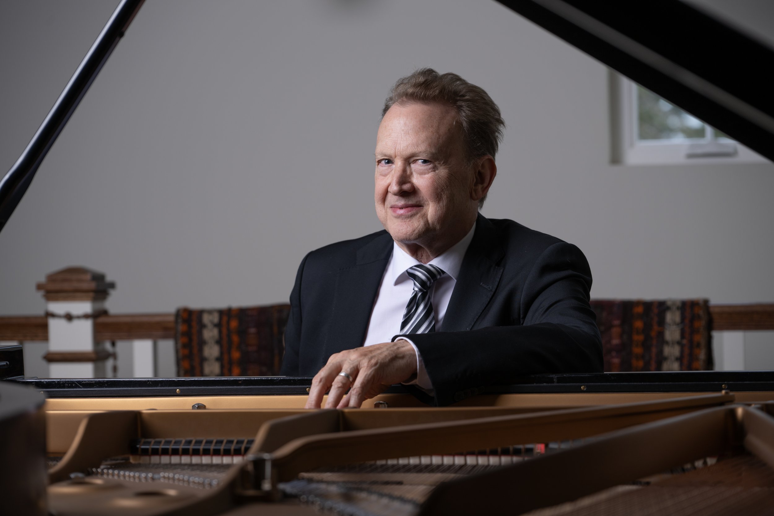 Peter Orth sitting at a grand Steinway piano smiling at the camera.