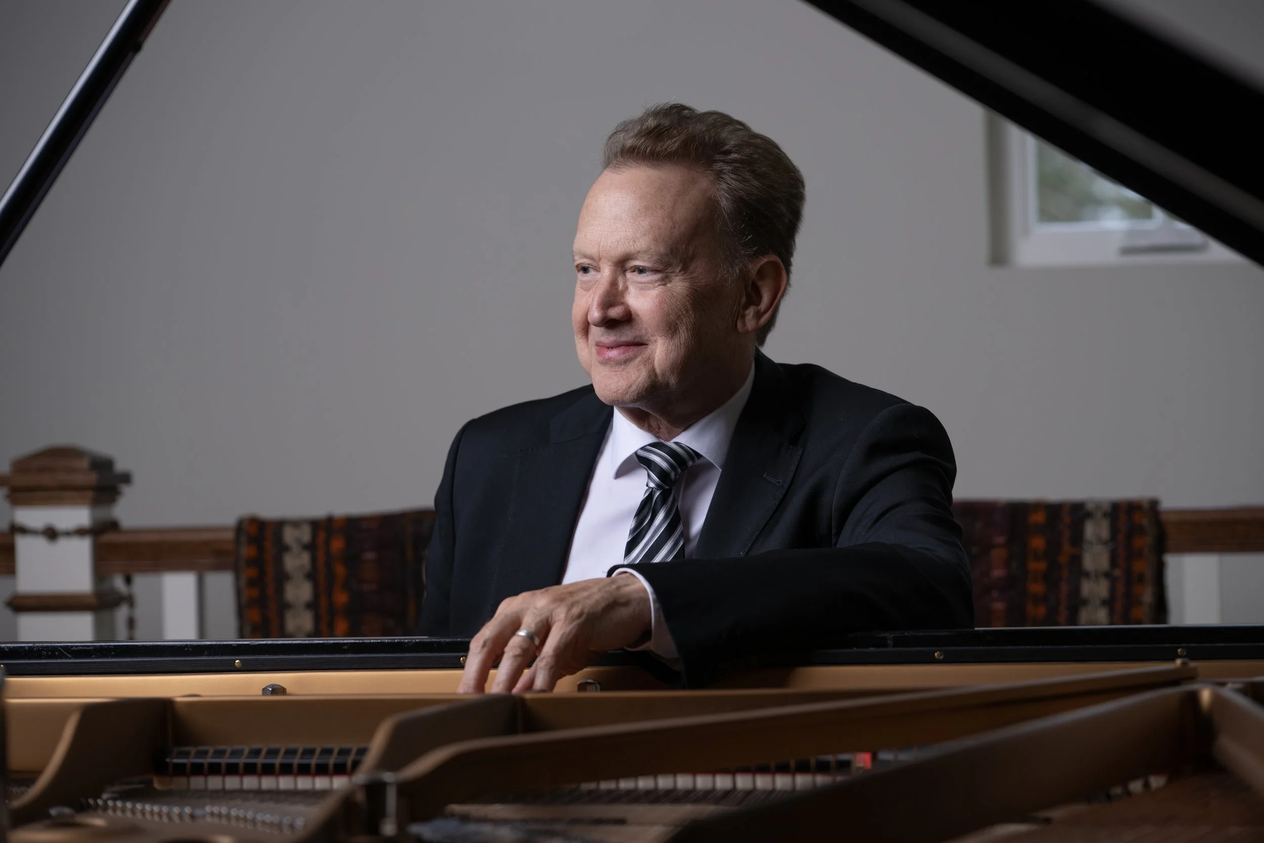 Peter Orth sitting at a grand Steinway piano smiling looking away from the camera.
