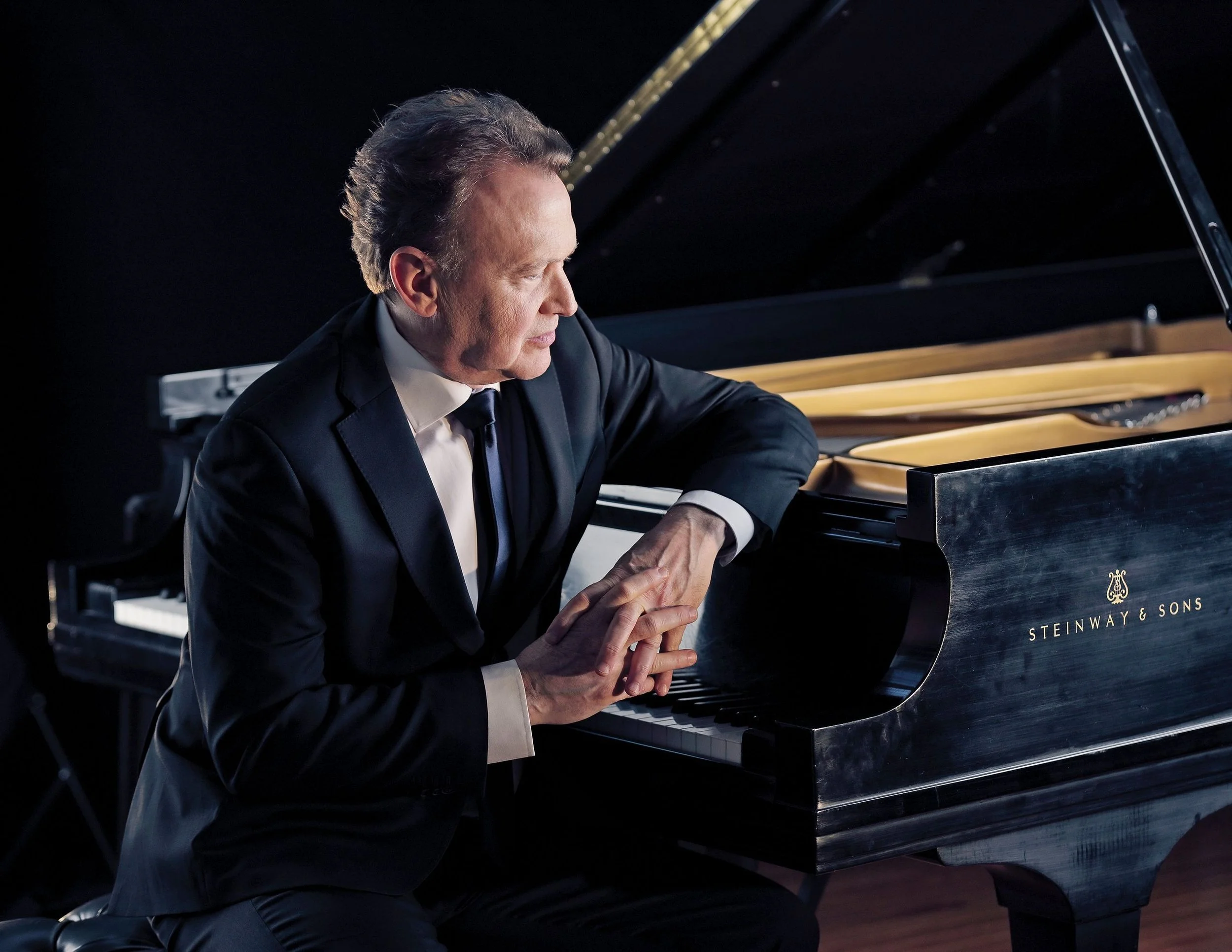 Peter Orth in a black suit playing a black grand piano with a focused expression.