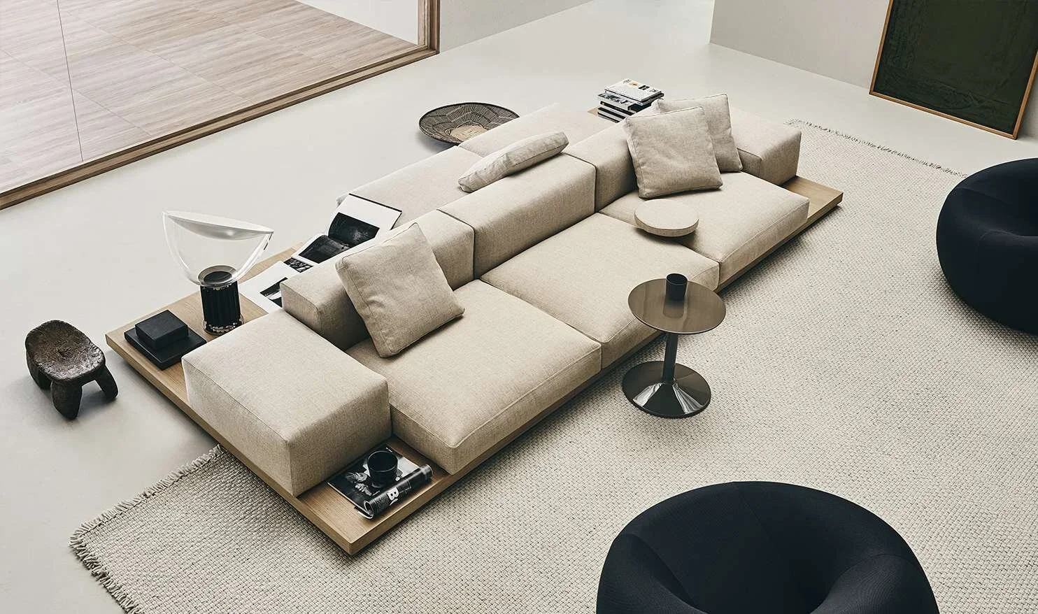A modern beige sectional sofa with throw pillows, a small side table, and various decorative items in a contemporary living room.