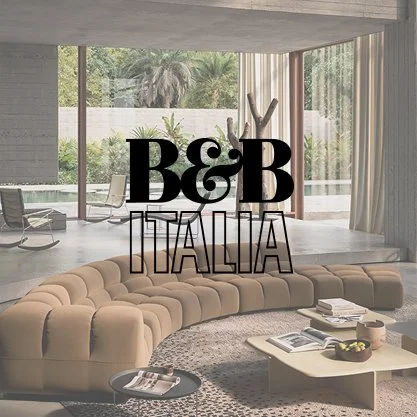 Modern living room with a large beige curved sofa, coffee table with magazines, and large windows showing greenery outside, with text overlay reading 'B&B Italia'.