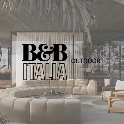 Modern outdoor lounge area with large beige sectional sofa, armchair, and coffee table, with a glass wall and trees outside, and a sign displaying B&B Italia Outdoor logo.