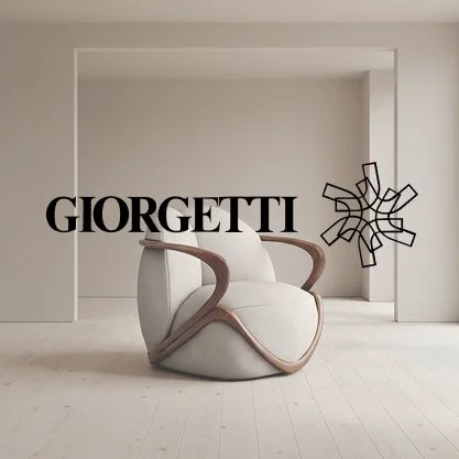 Modern white armchair with wooden armrests in a minimal white room with the word 'Giorgetti' and a wire decorative piece on the wall.