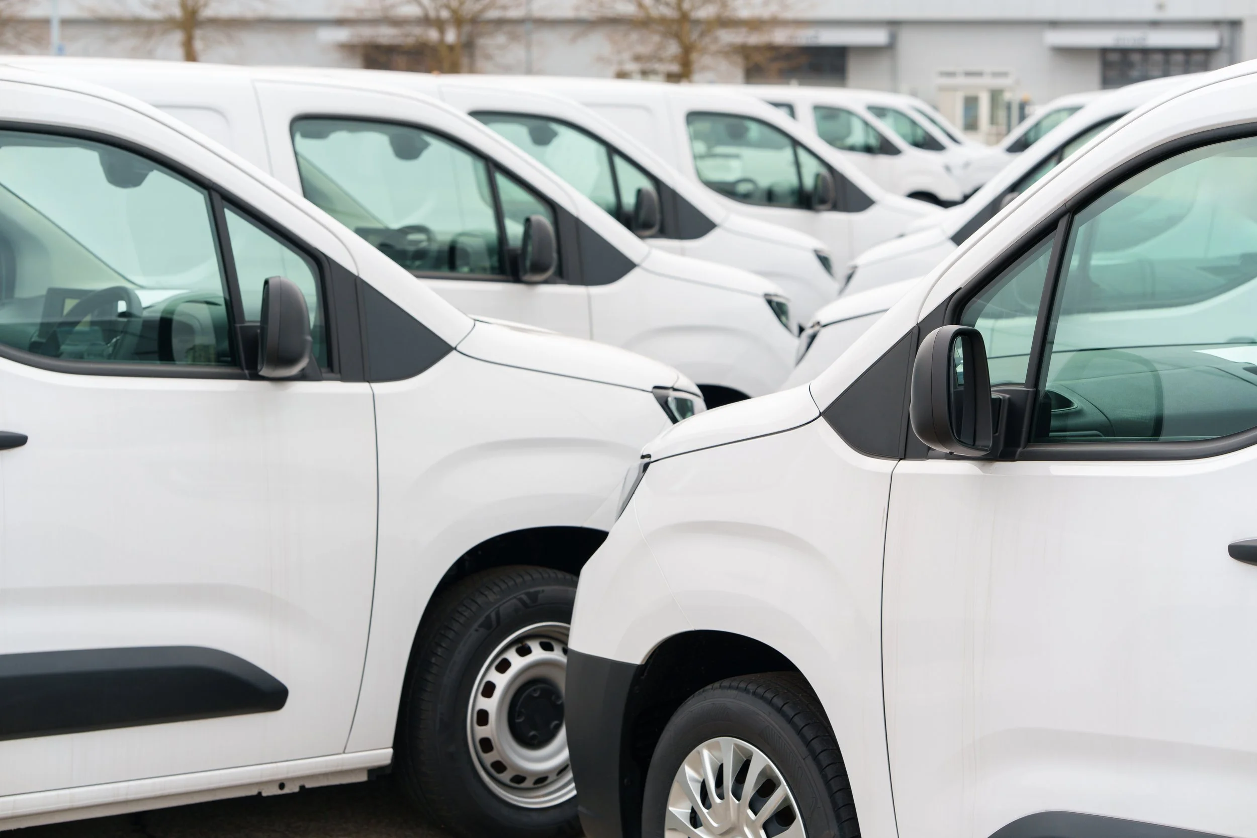 Multiple white commercial vans parked in a lot, viewed from the side.