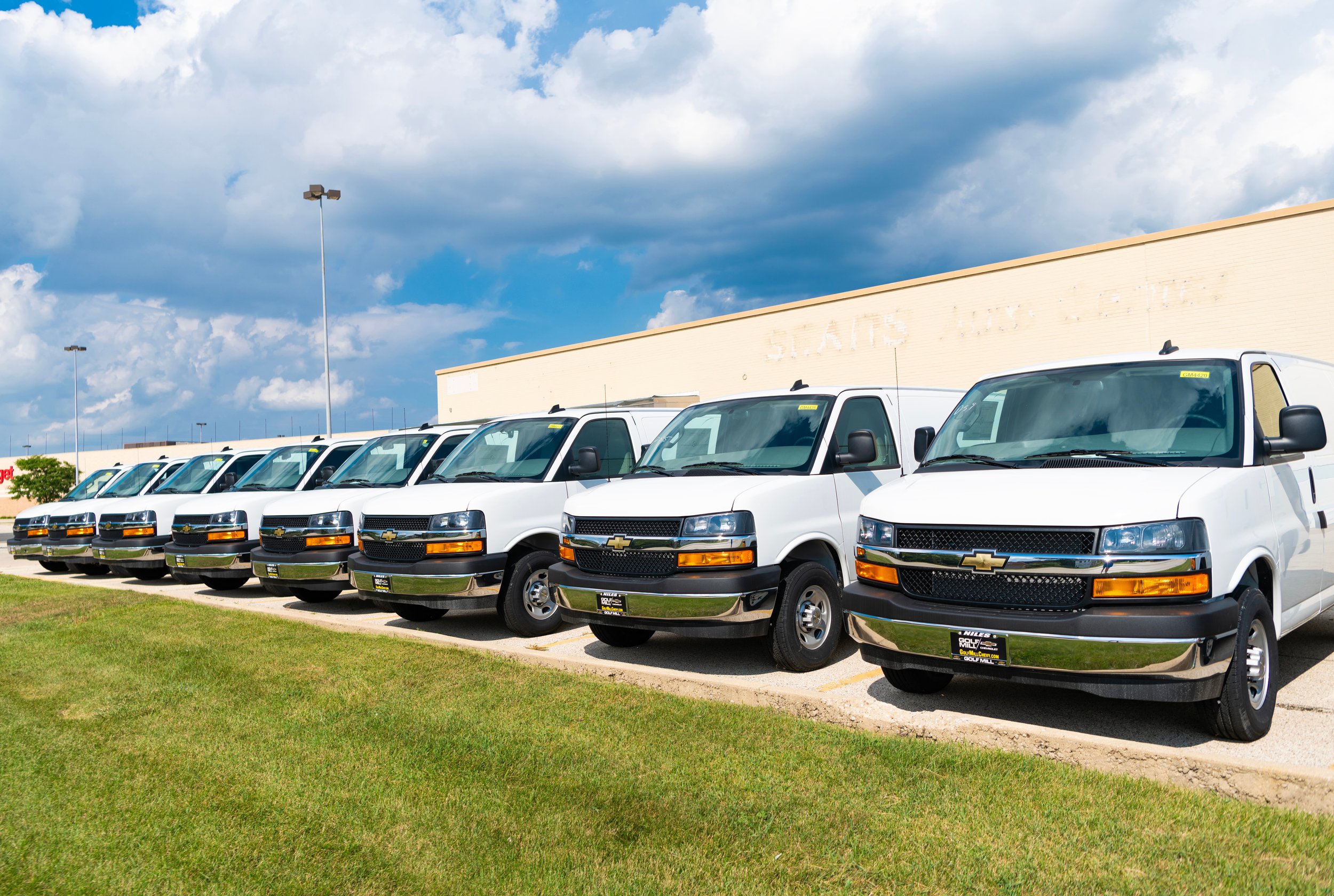 White Chevrolet vans parked in a row outside a building under a partly cloudy sky.