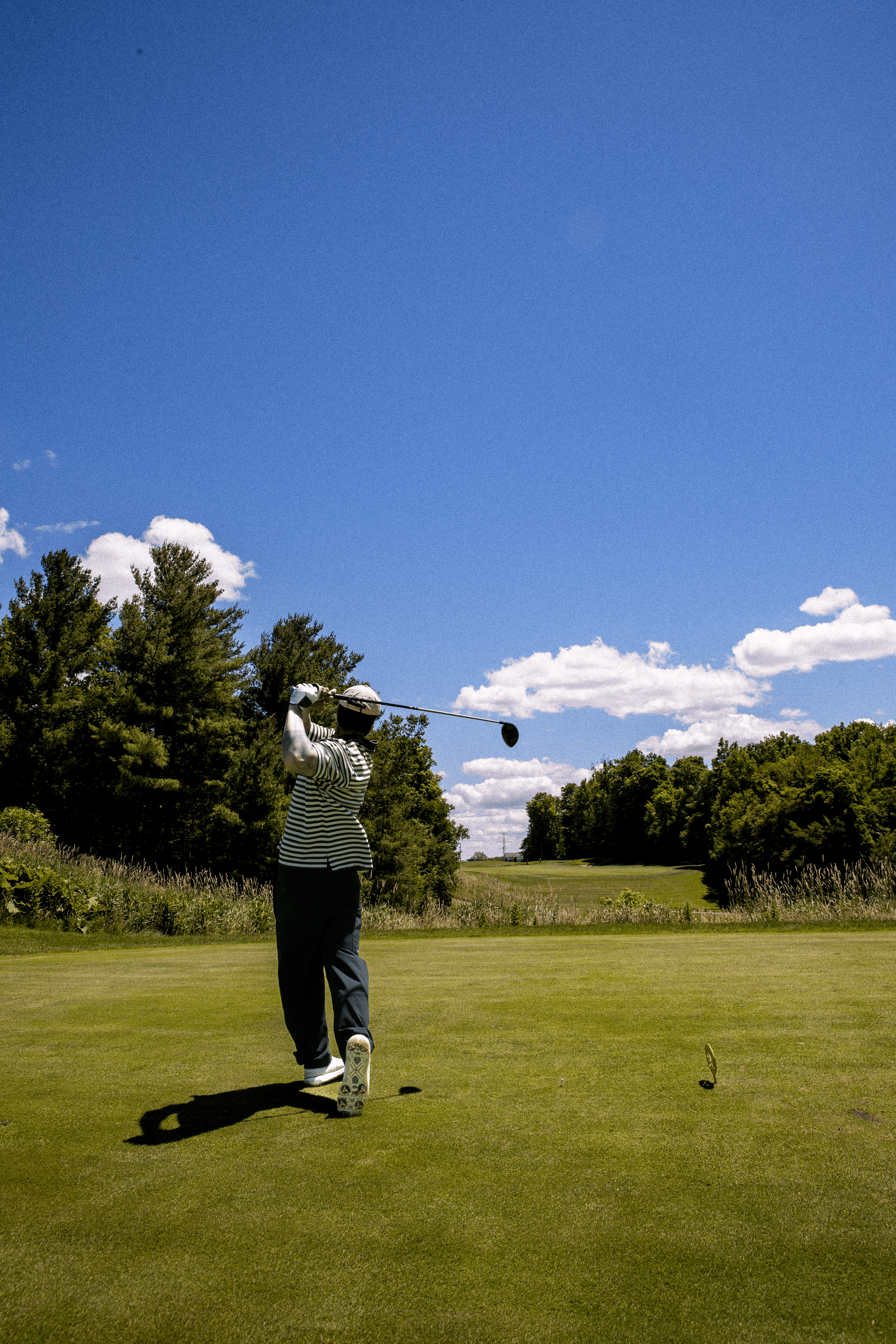 A person wearing a hat and striped shirt is swinging a golf club on a golf course.