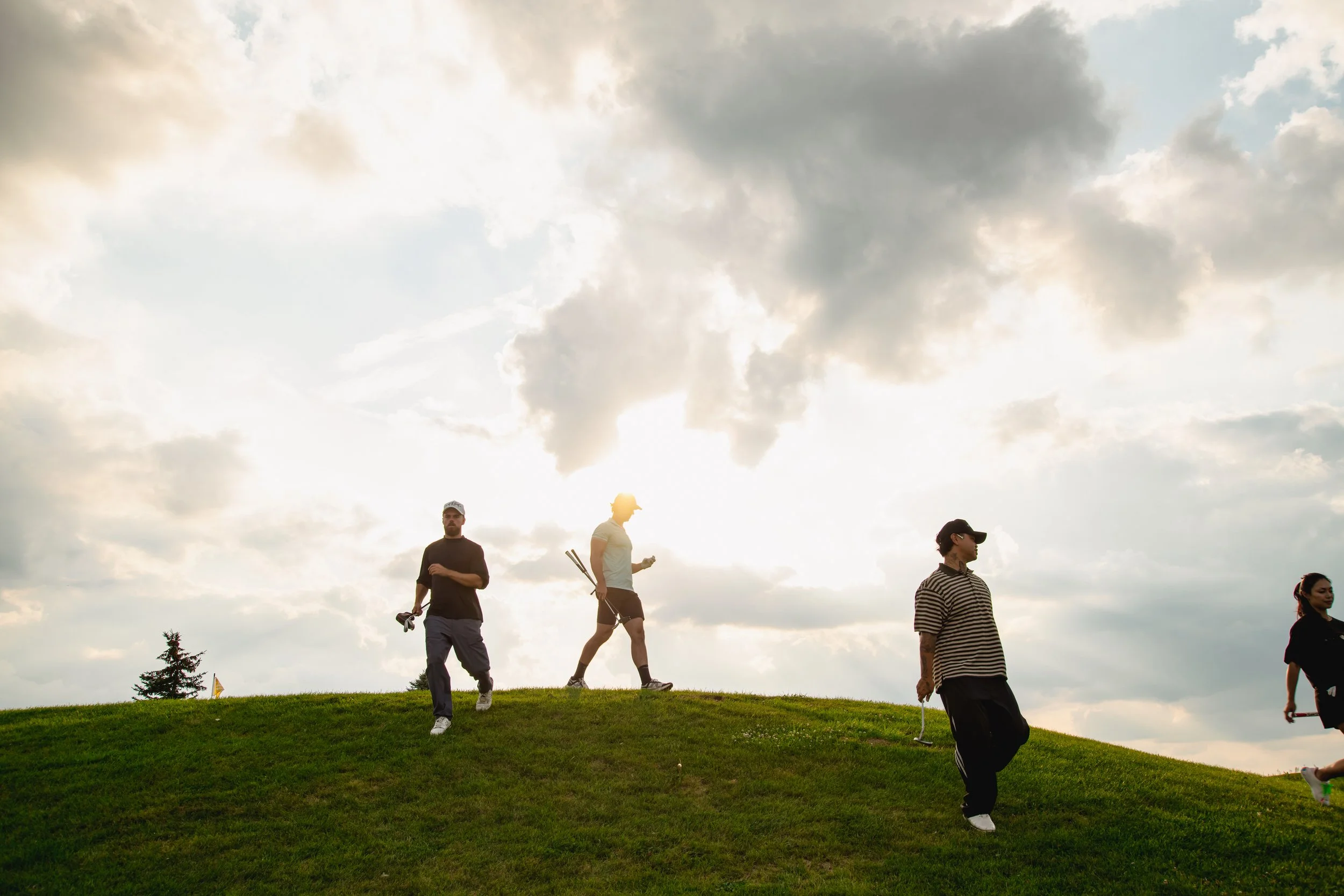 Group of people walking on grass hill under cloudy sky during daytime.