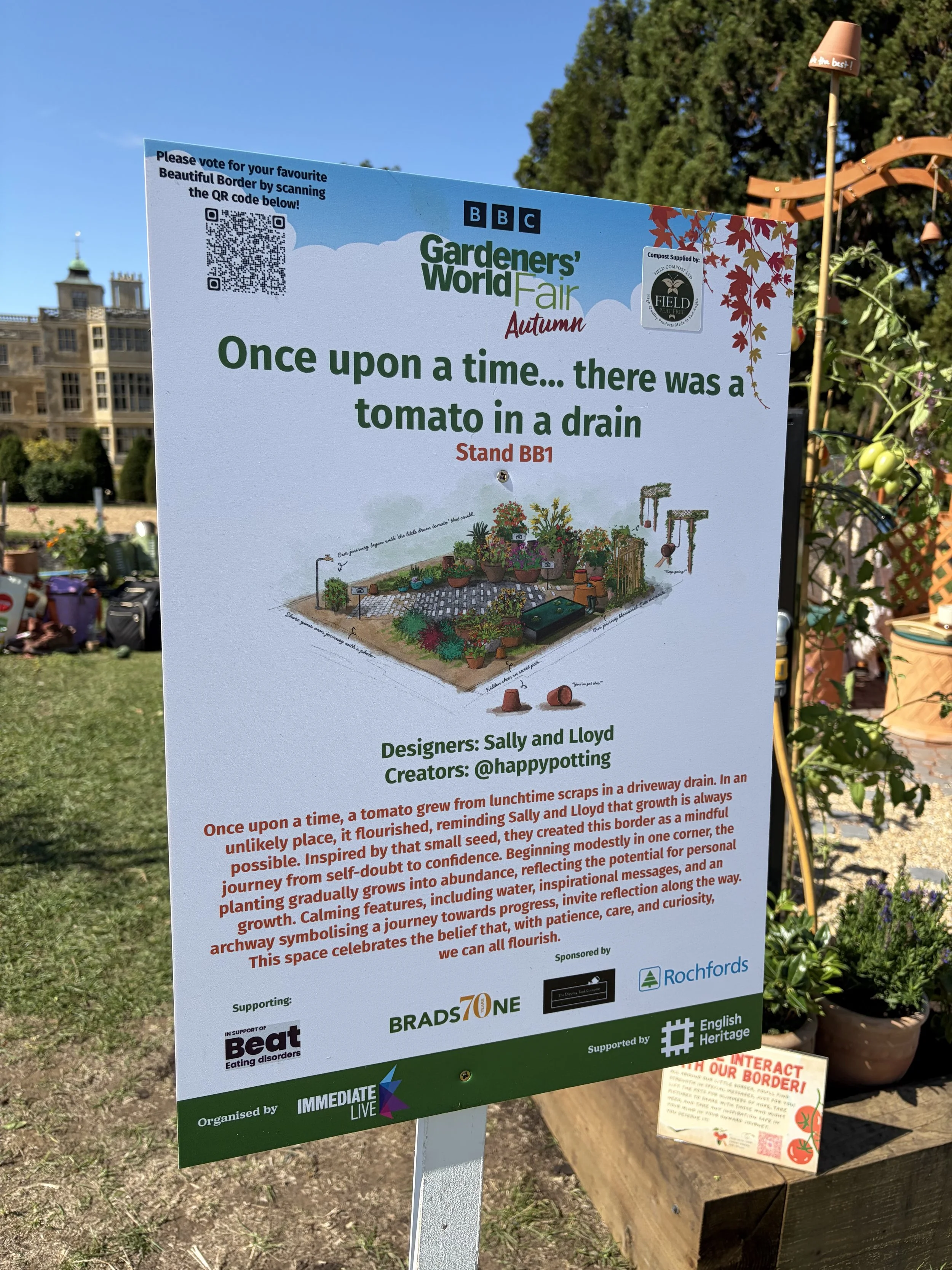 Sign at Gardeners' World Fair Autumn event with a QR code, event details, and artwork of a garden with plants and garden tools, promoting voting for favorite border design.