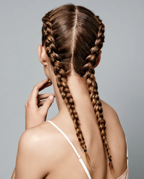 Side profile of a woman with red hair styled in two Dutch braids.