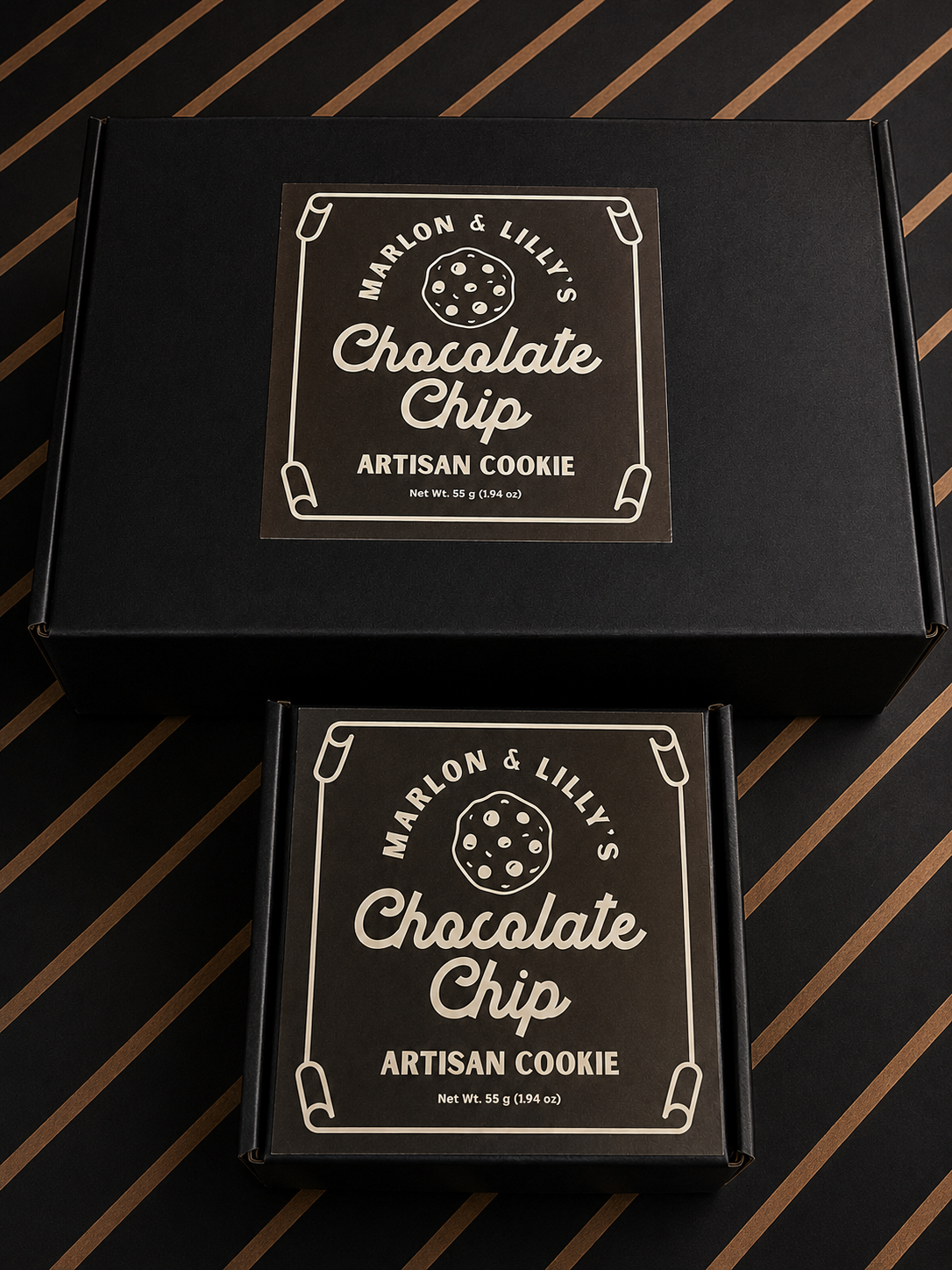 Two black boxes labeled 'Marlon & Lilly's Chocolate Chip Artisan Cookie', with a cookie graphic, placed on a black and gold striped surface.
