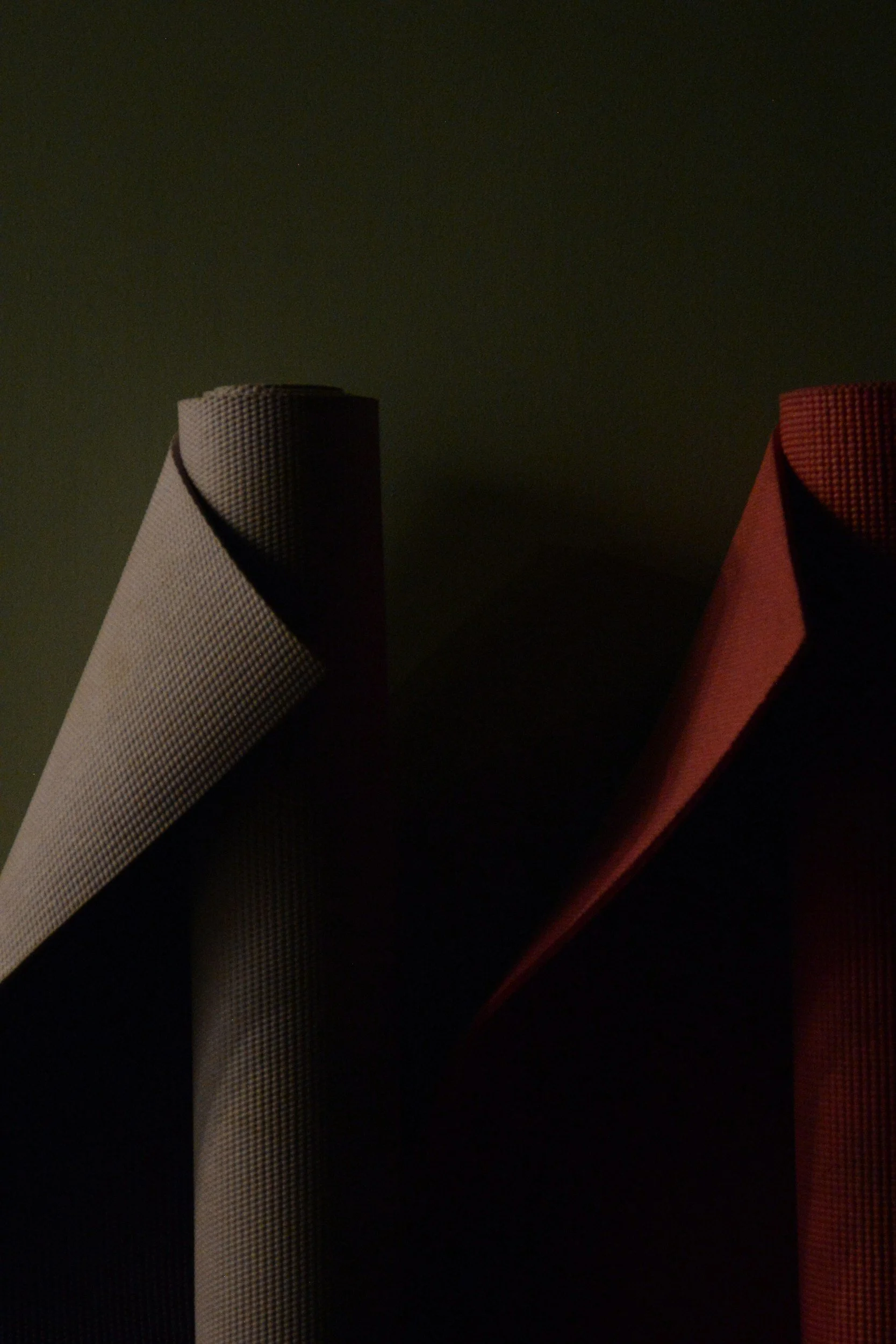 Close-up of three yoga mats in gray, black, and red colors set against a dark background.