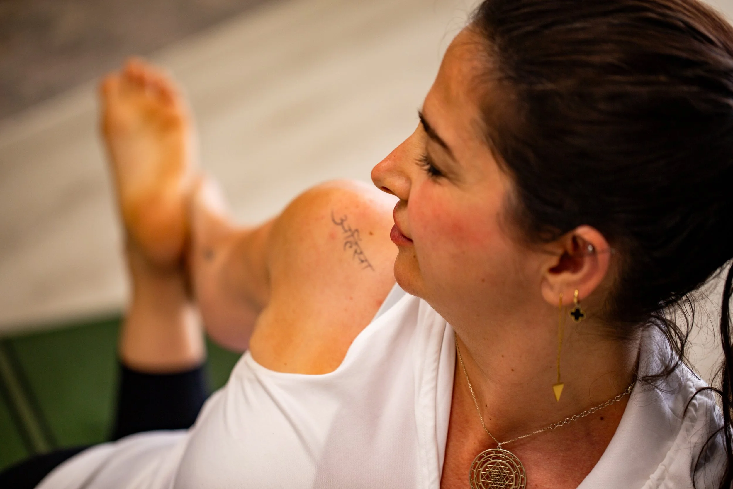 A woman with dark hair and earrings, doing a yoga pose with her eyes closed, in a close-up shot.