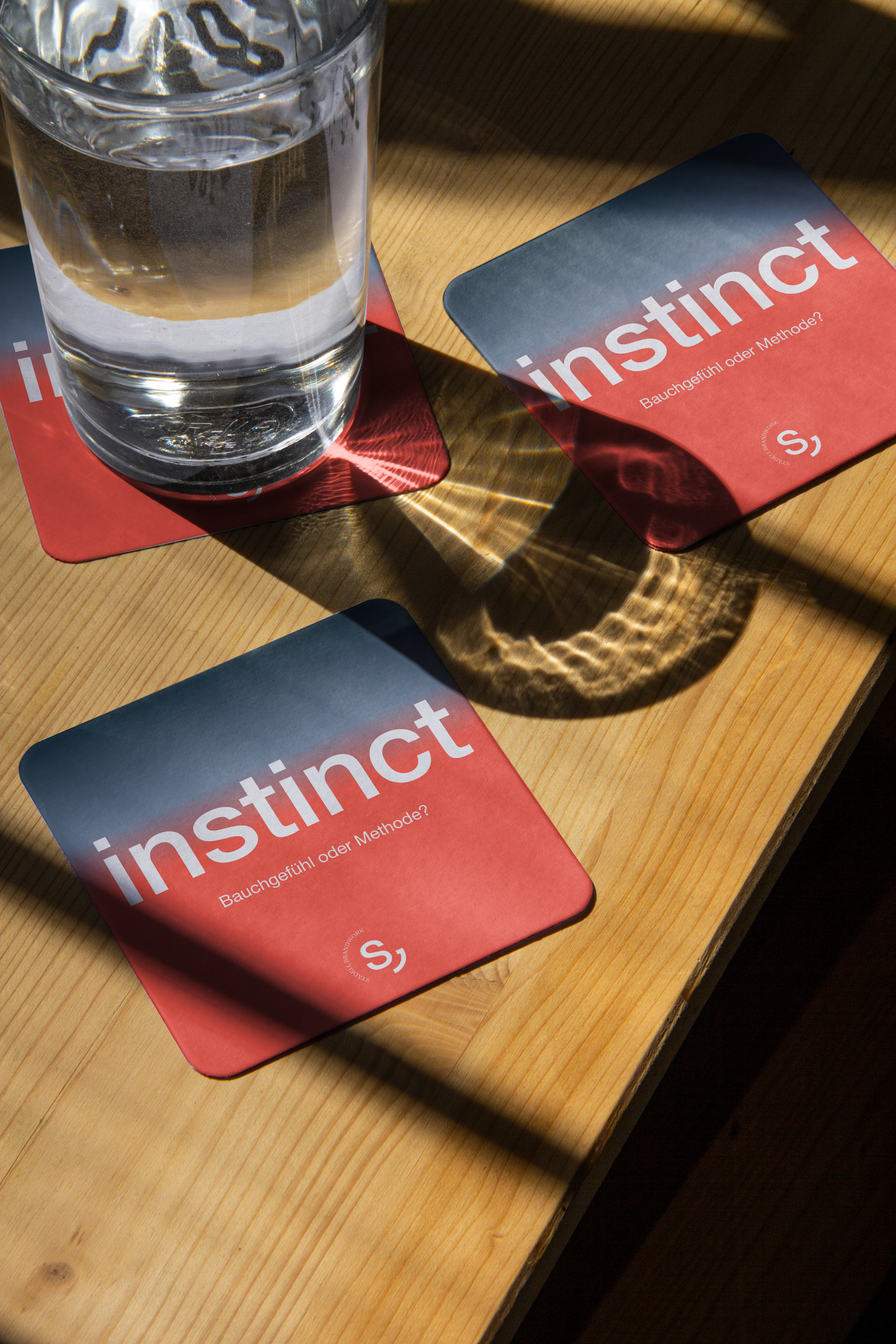 Ein Glas Wasser auf einem roten Untersetzer neben einem roten Buch mit dem Titel 'instrukt' auf einem Holztisch.