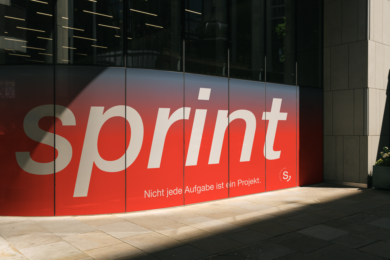 Außenansicht eines modernen Gebäudes mit großem Fenster und einer Werbetafel mit der Aufschrift 'sprint' und dem Satz 'Nicht jede Aufgabe ist ein Projekt.'.