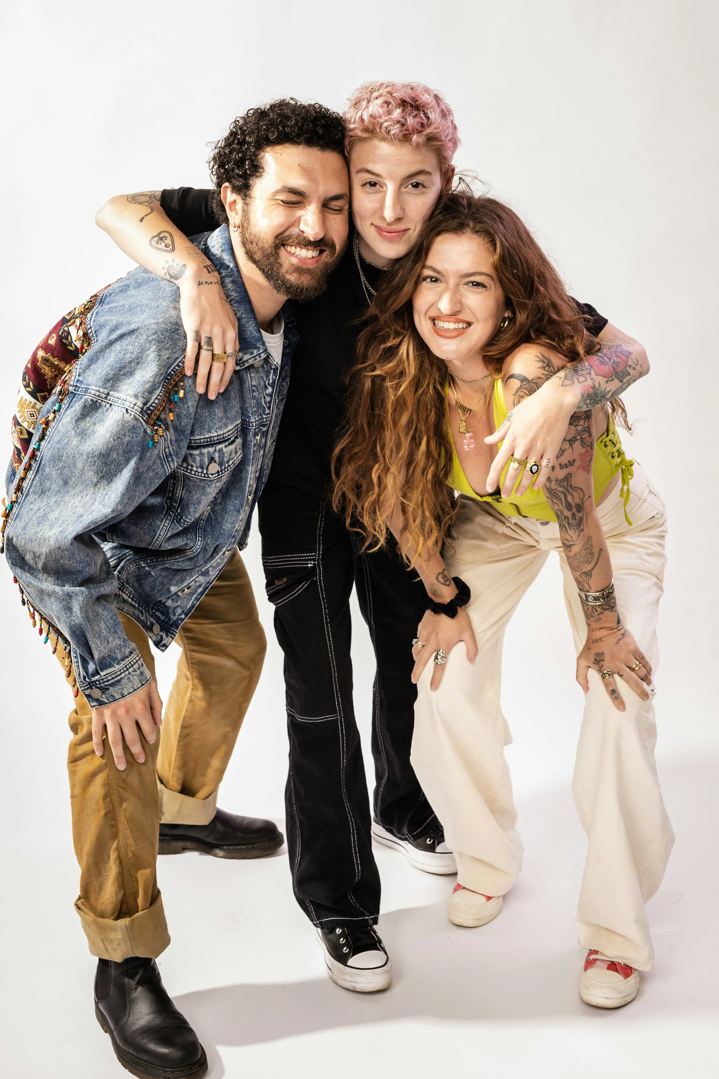 Three diverse friends smiling and hugging against a plain white background.