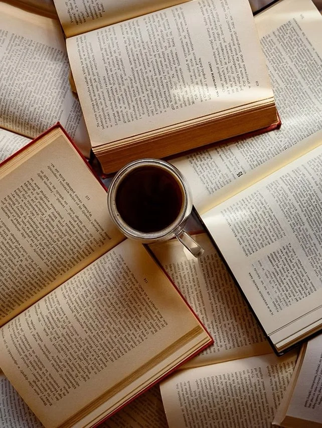 Several open books scattered around a table with a cup of black coffee in the center.