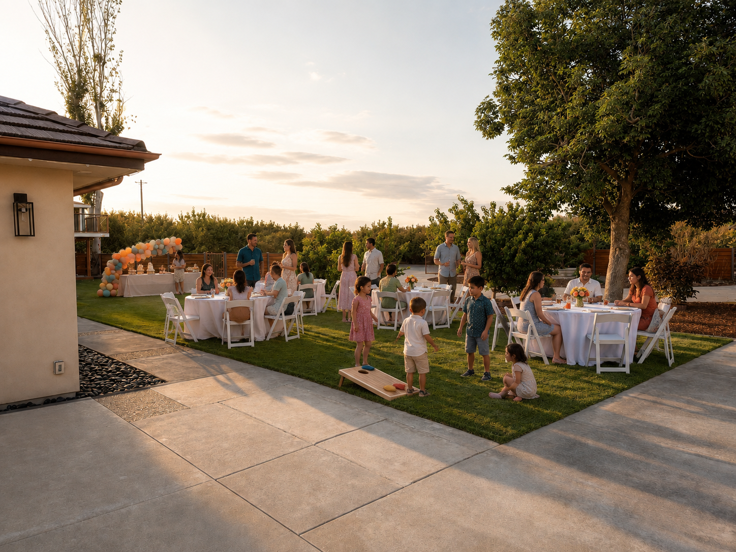People celebrating a birthday outdoors in a backyard with tables, chairs, and balloons, during sunset.