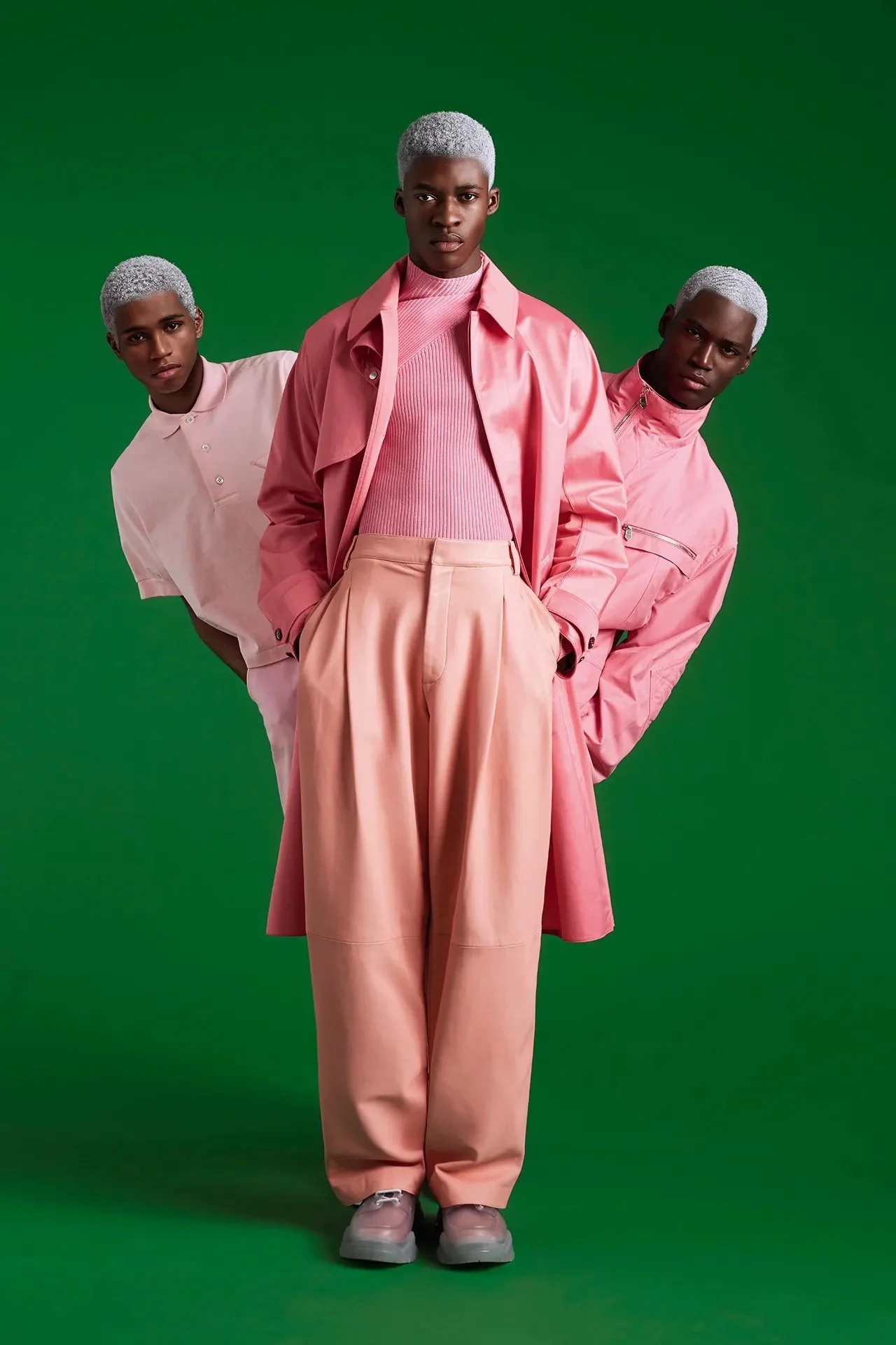 Three men dressed in tones of pink against a green background.