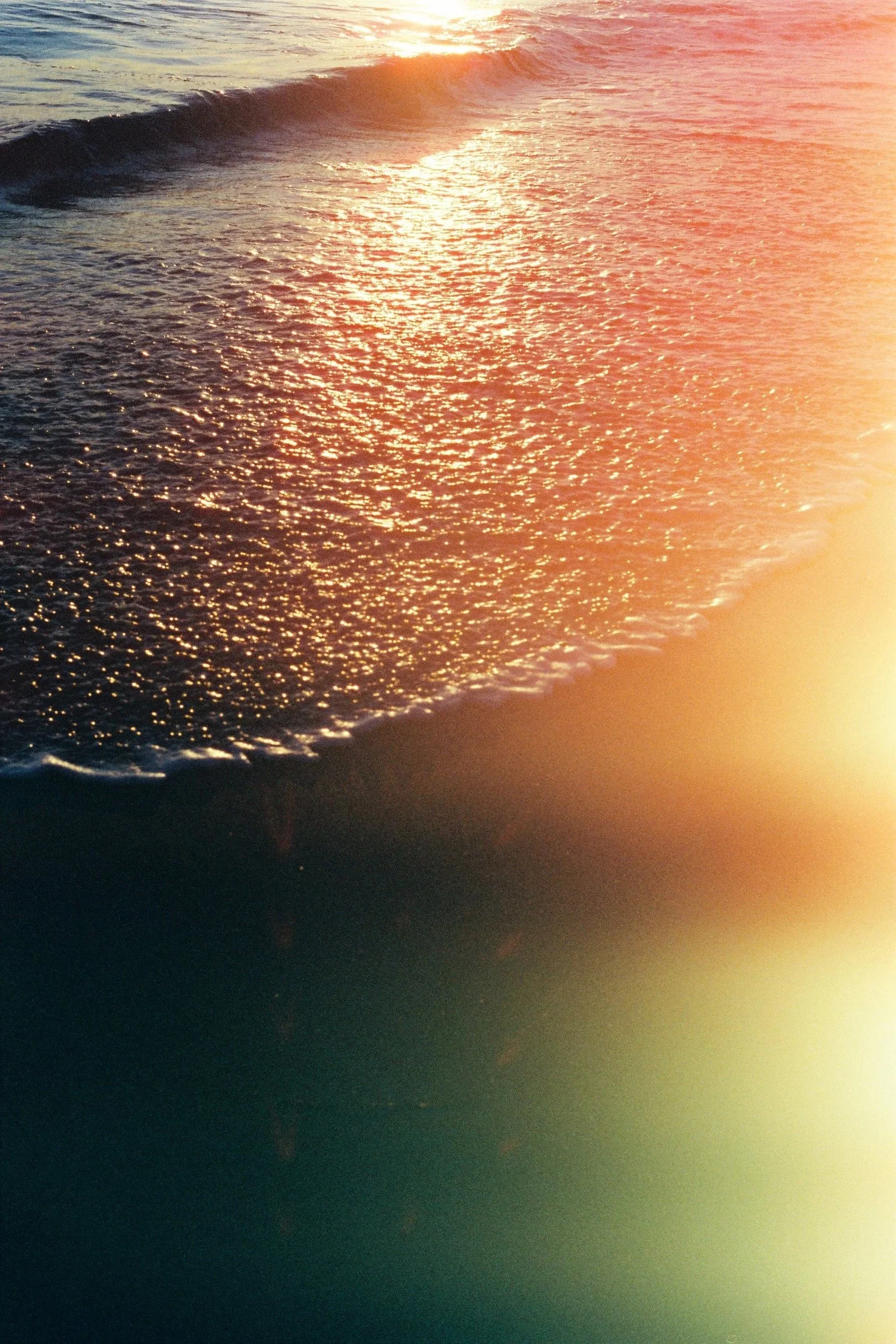 Sunset over the ocean with waves gently rolling onto the shore, reflecting the warm orange and golden hues of the setting sun.