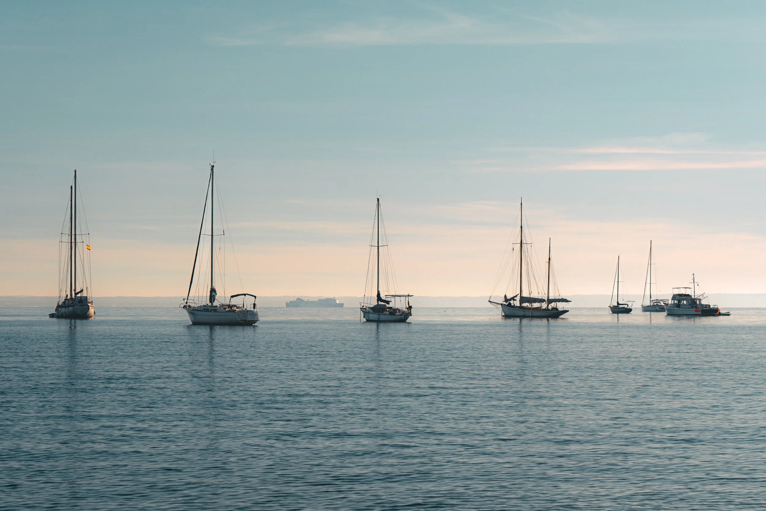 Sailboats and yachts on calm water at sunrise